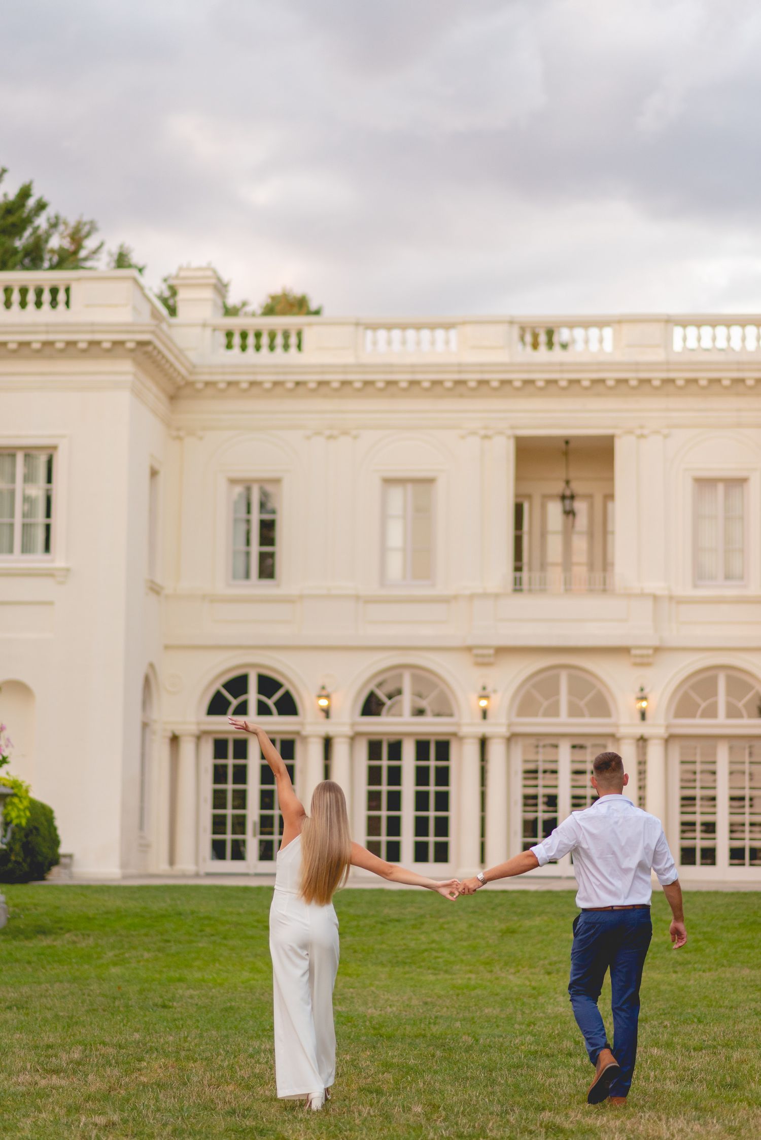 Couple walking playfully on the lawn in front of a grand white Wadsworth Mansion.
