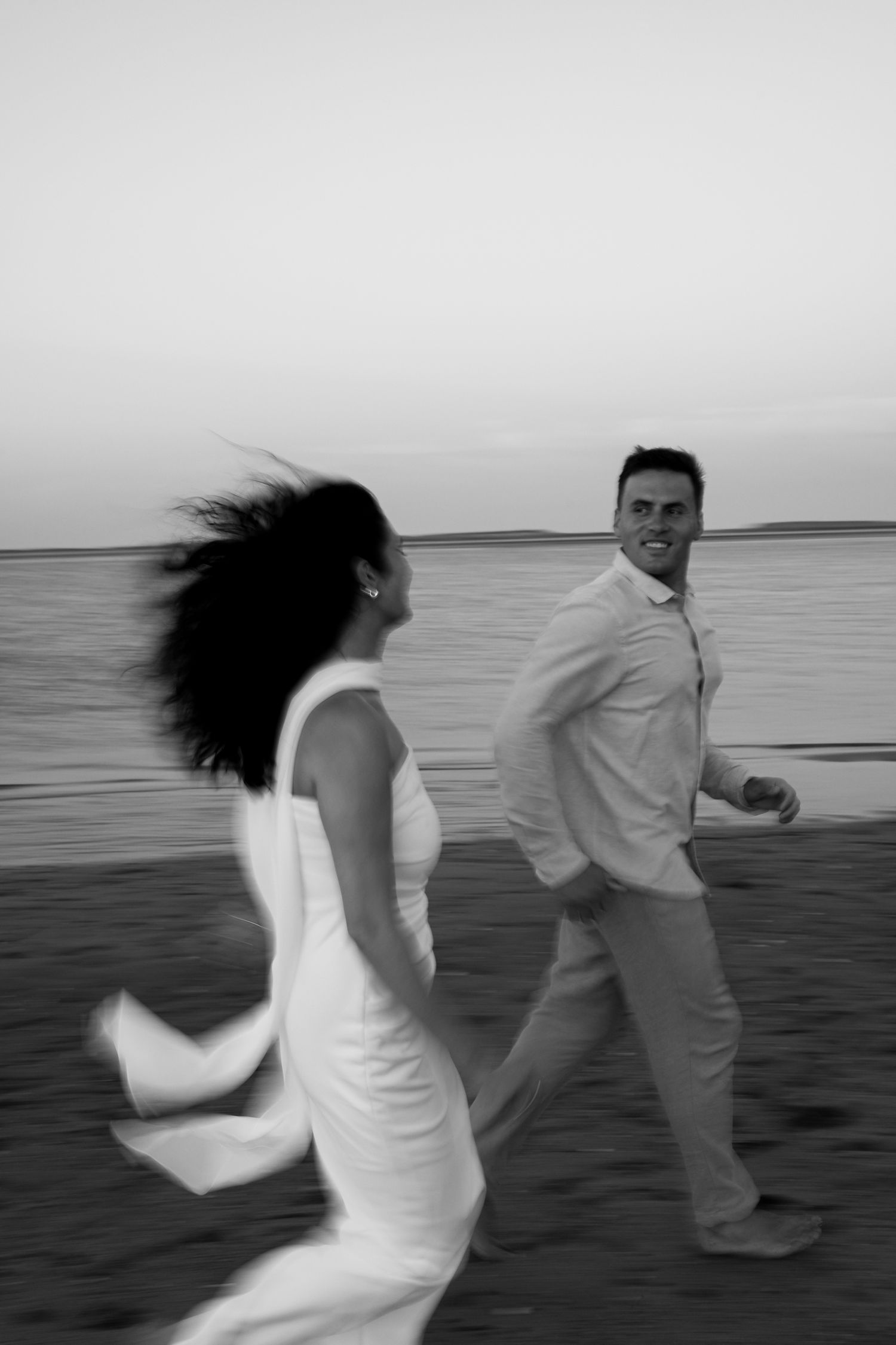 Black and white photo of a couple playfully running on a beach at sunset in Cape Cod.