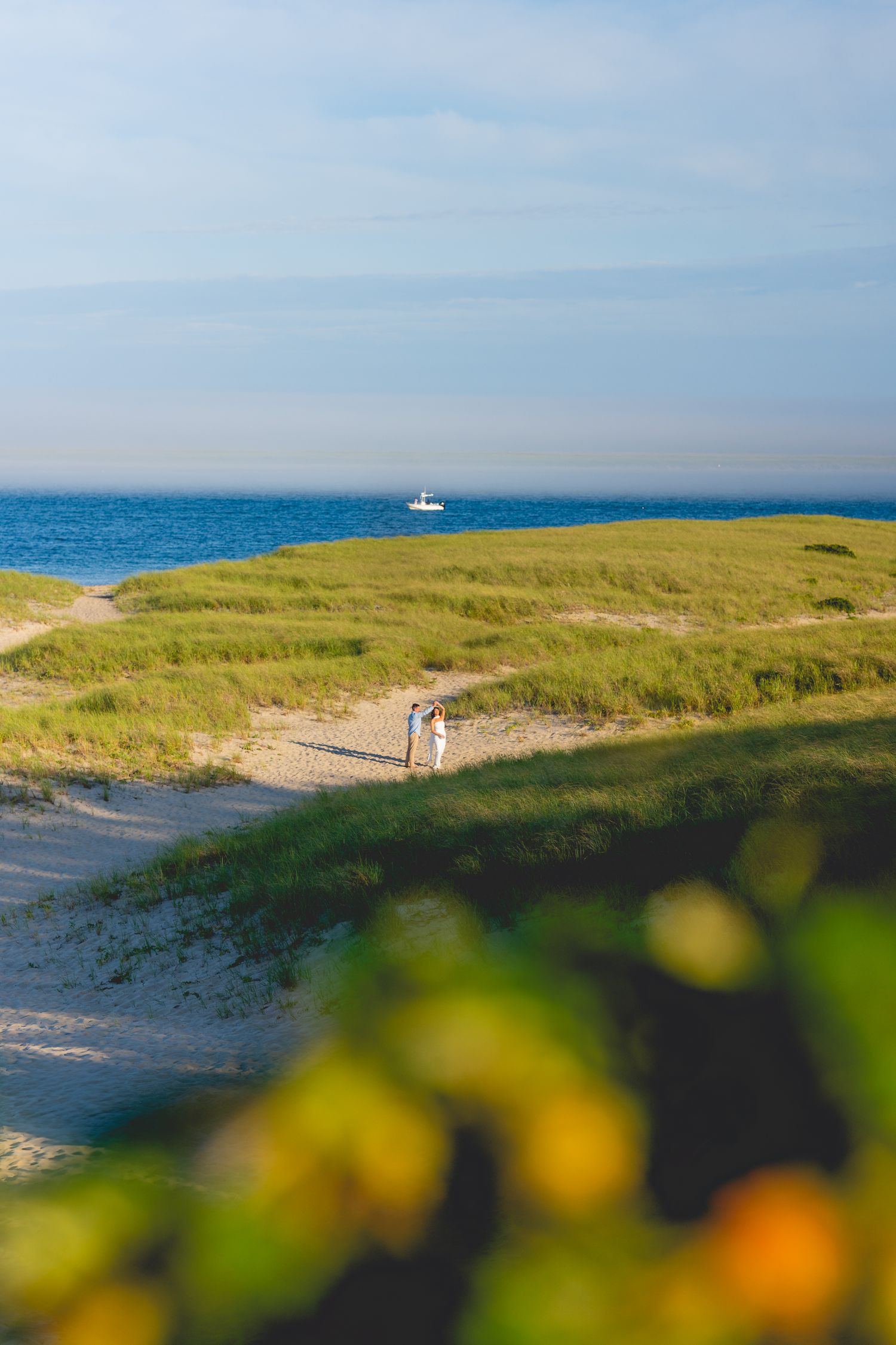 Coastal landscape with green dunes, sandy paths and blue ocean views at Chatham Lighthouse Beach in Chatham, Massachusetts.