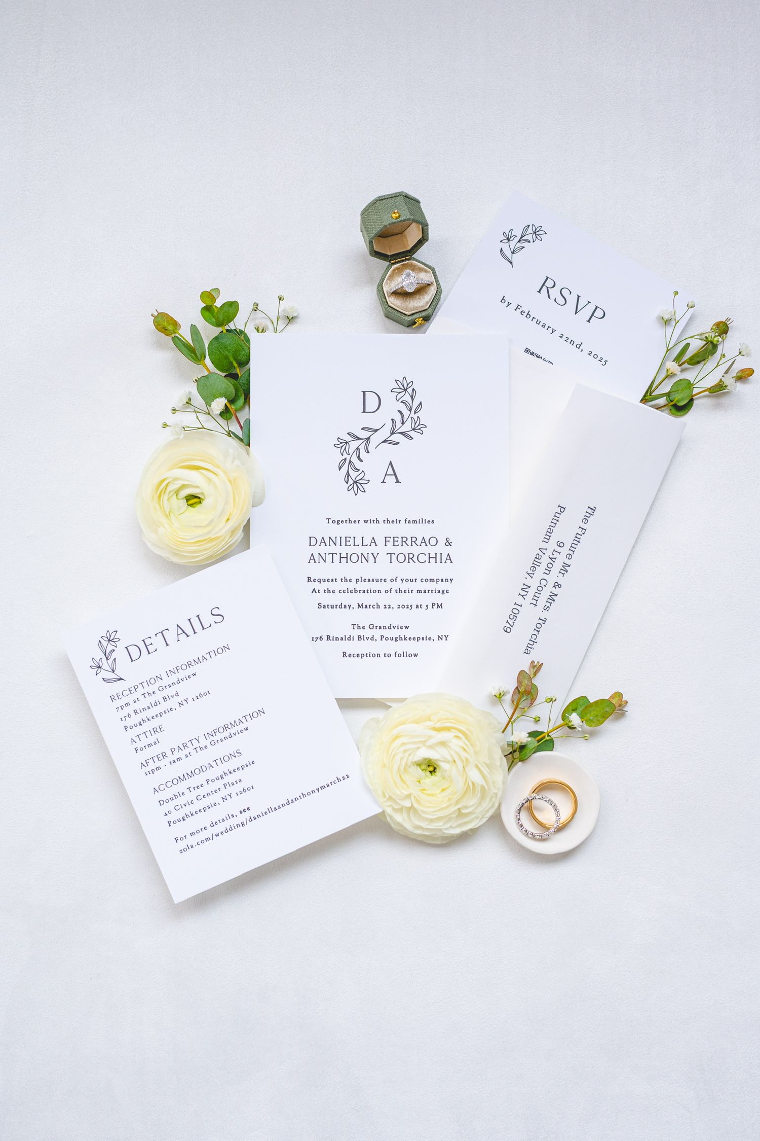 Elegant wedding invitation suite with white ranunculus flowers and greenery on light background.