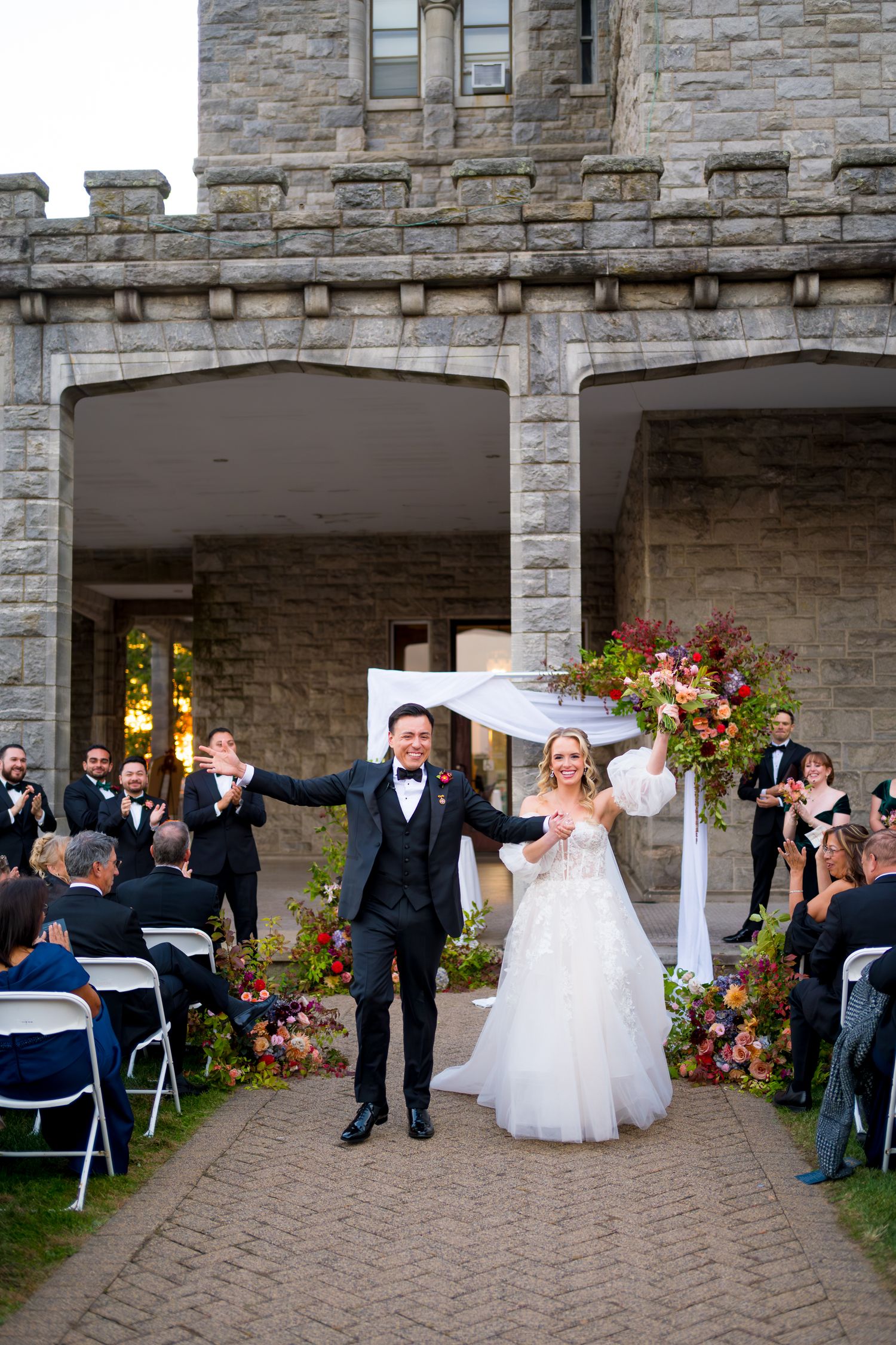 Wedding ceremony sequence showing guests gathered at a stone castle venue with elegant floral arrangements and outdoor seating.