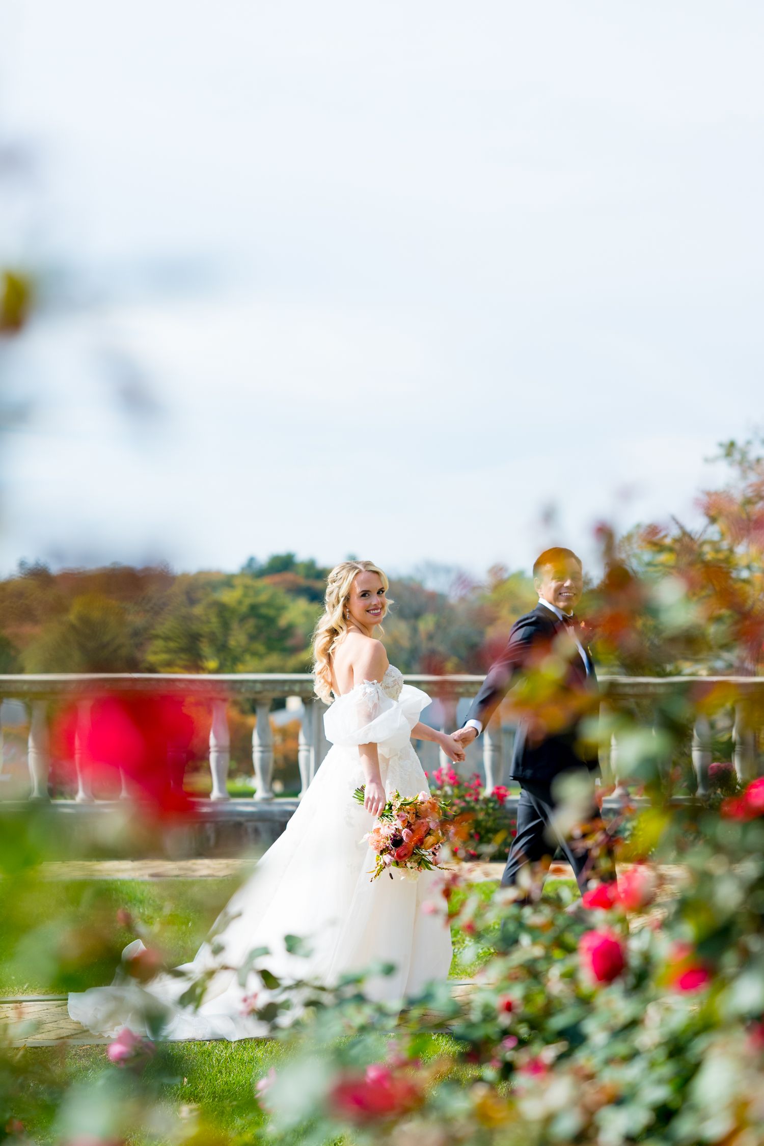 A couple on a scenic balcony surrounded by blooming red roses and autumn foliage on their wedding day.