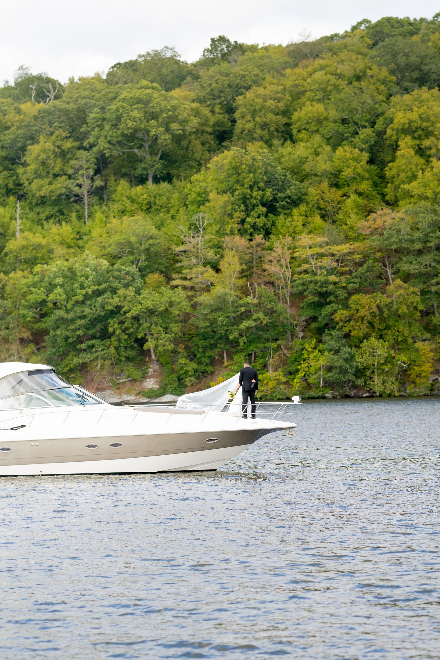 Two white speedboats cruise along a lake surrounded by lush green forested shoreline.