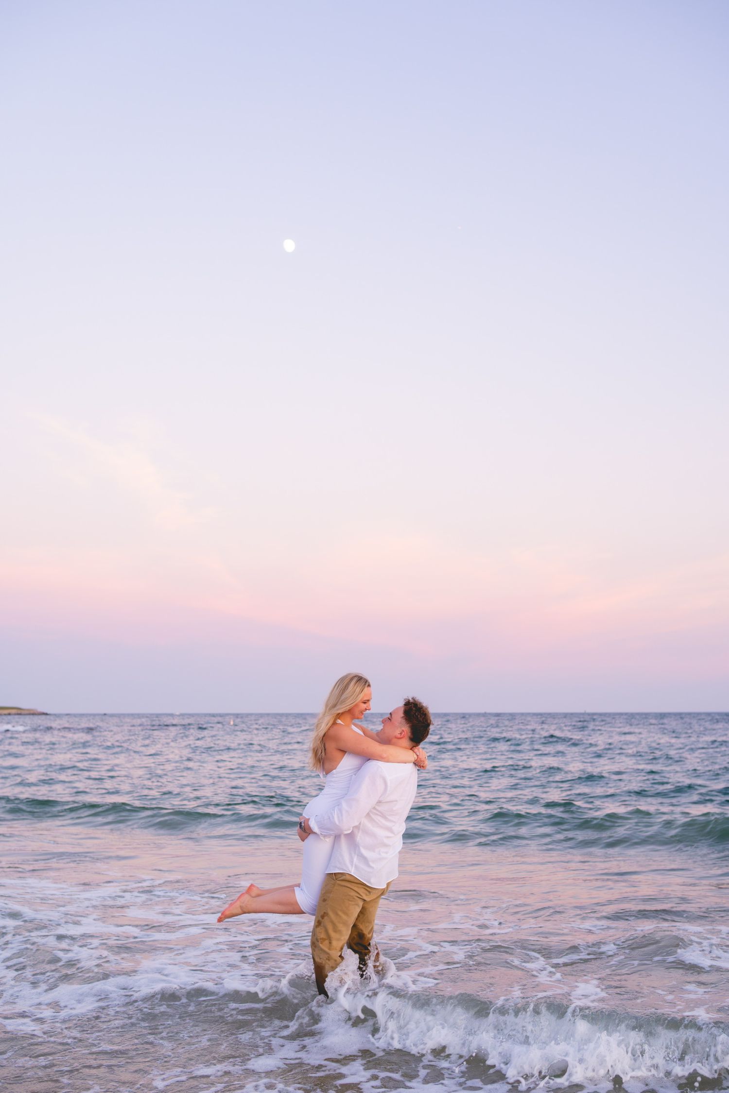 A romantic couple plays in the ocean waves during sunset in Watch Hill, Rhode Island.