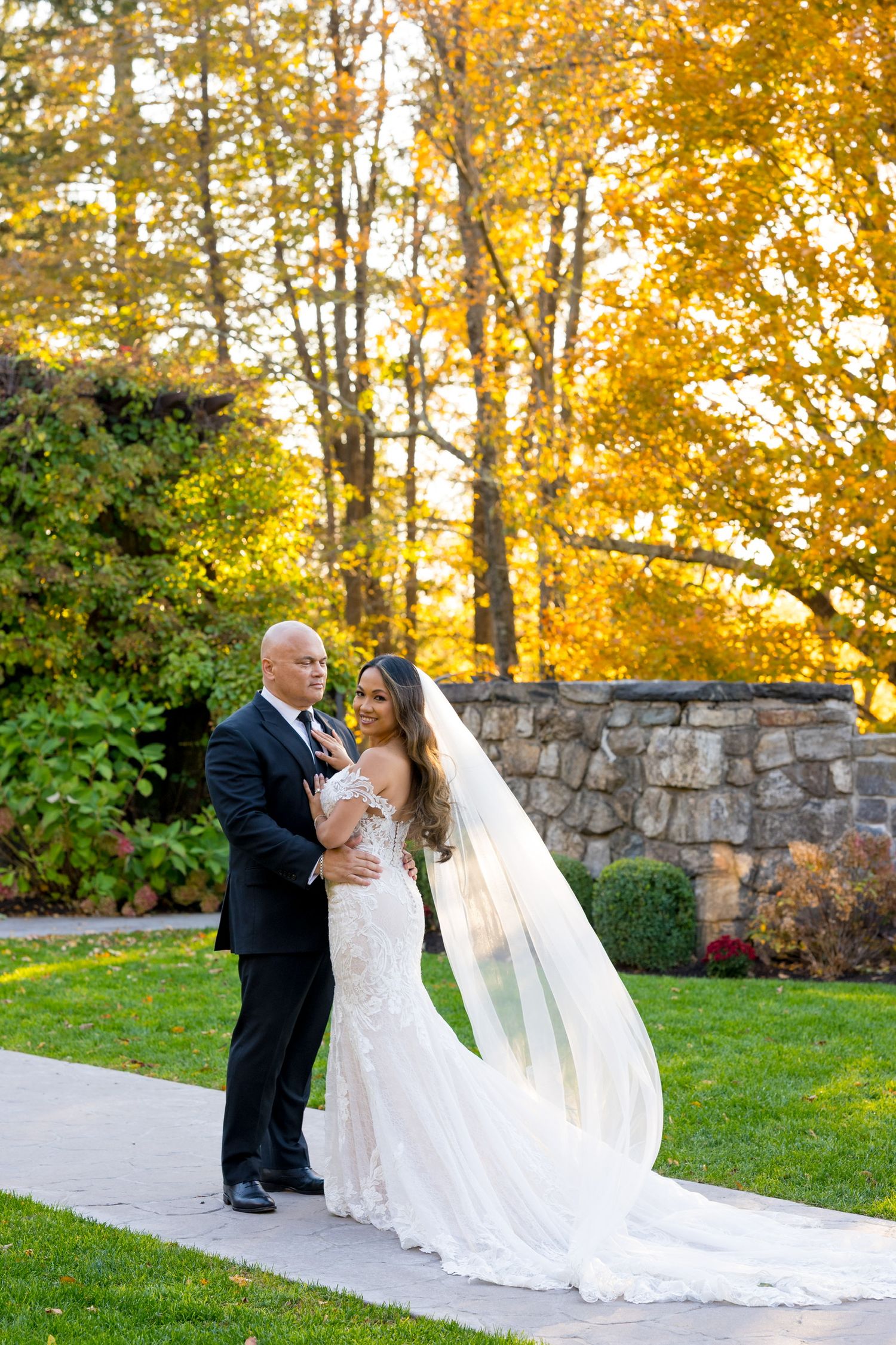 A wedding couple shares a tender moment on a stone path surrounded by autumn trees at Le Chateau in Westchester County, New York.