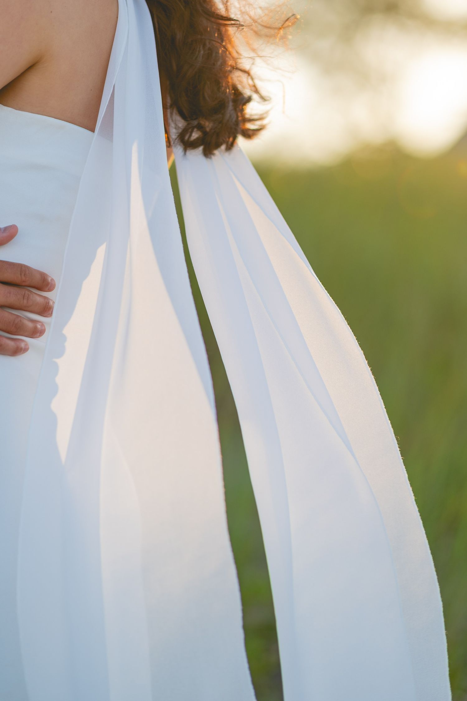 Close-up details of flowing white fabric from a dress against a soft blurred background.