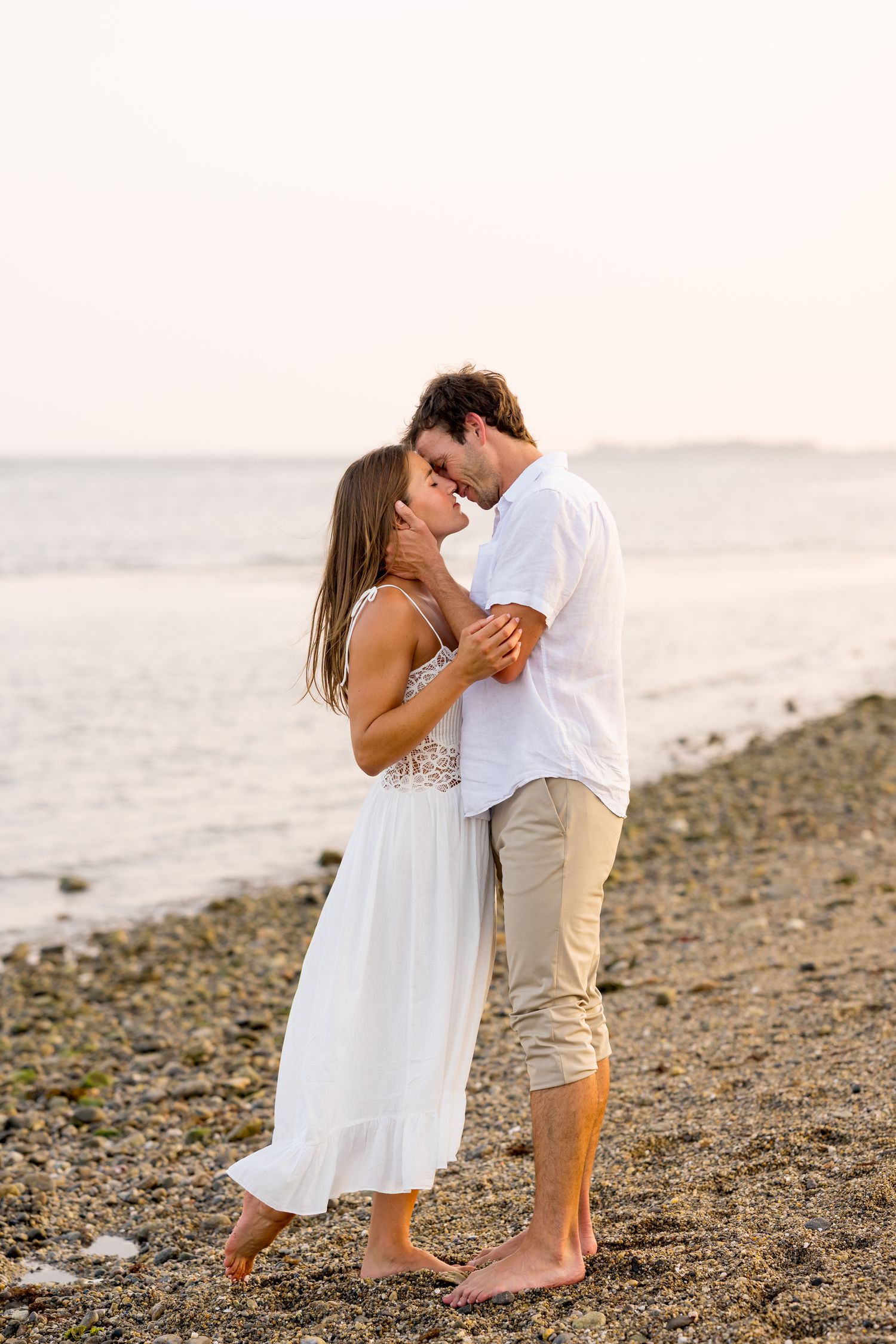 Romantic beach scene with couple embracing on rocky shoreline at sunset.