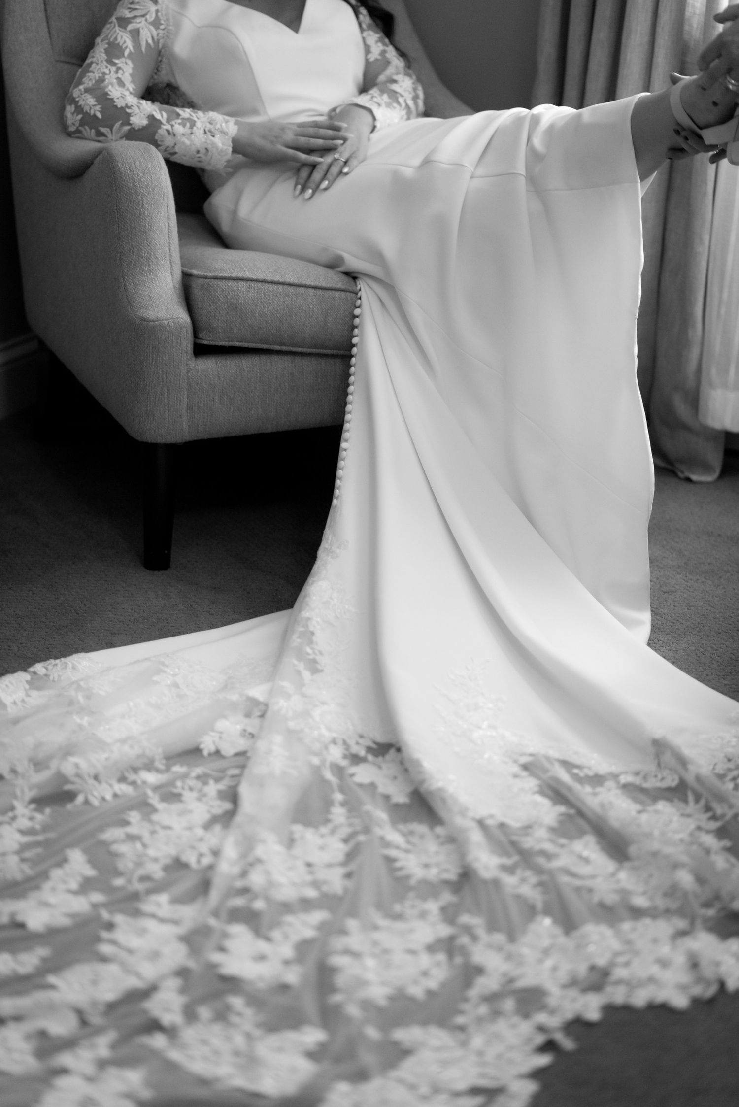 Intricate lace details of a white wedding dress train spread across a gray floor.