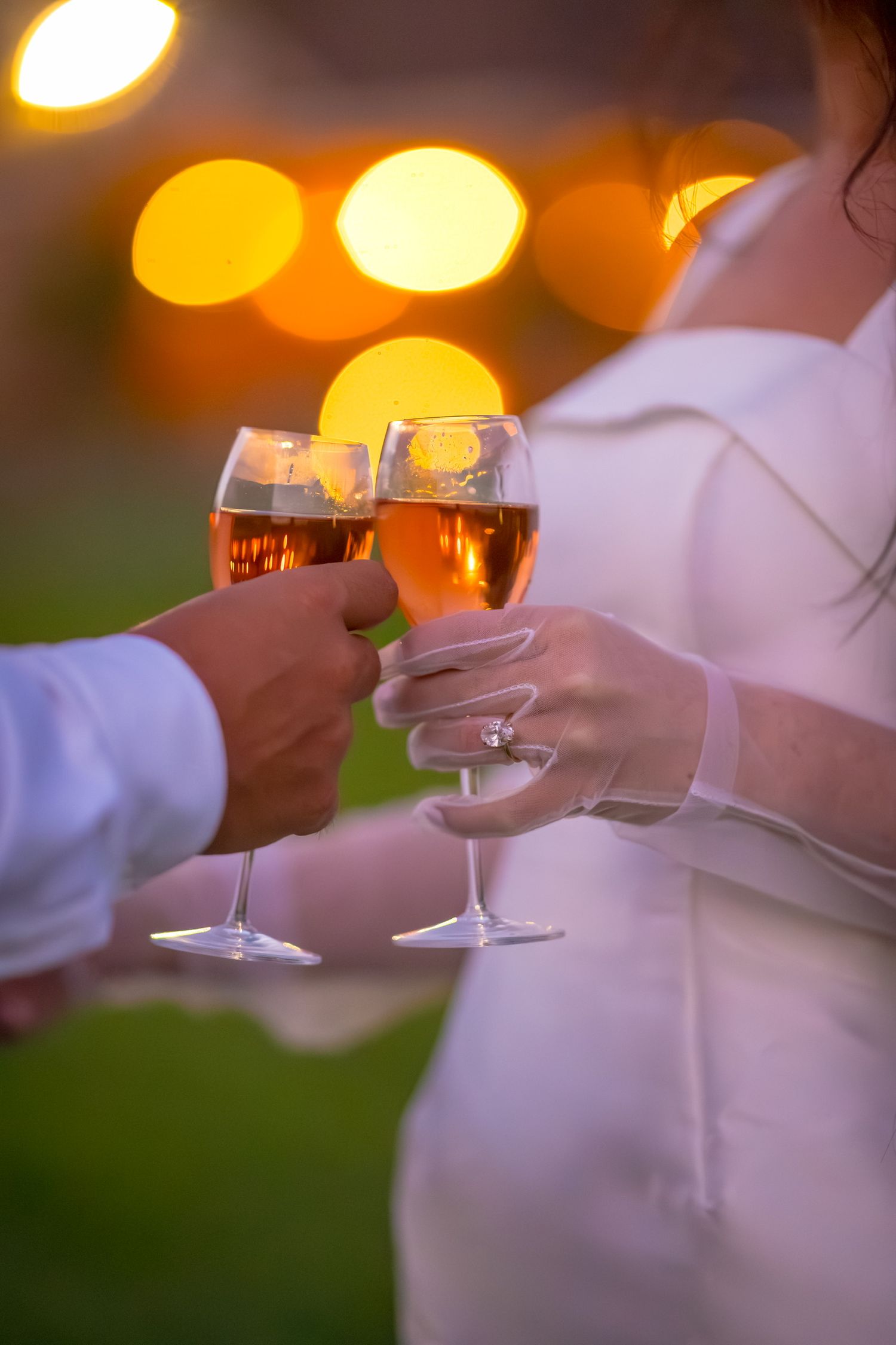 Wine glasses clink together in an evening toast with warm bokeh lights in background.