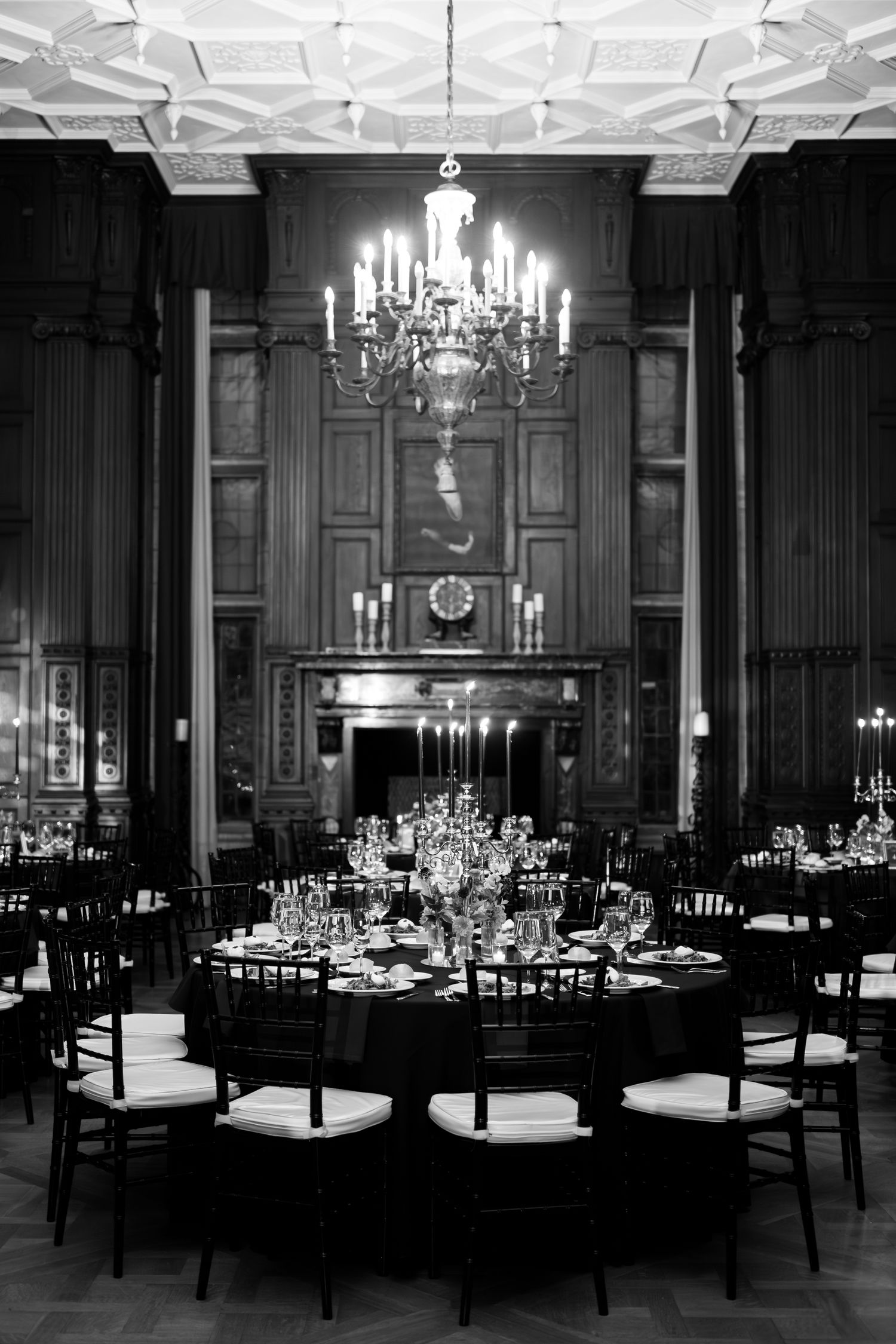 Elegant banquet hall setup with chandeliers and formal table settings in black and white.