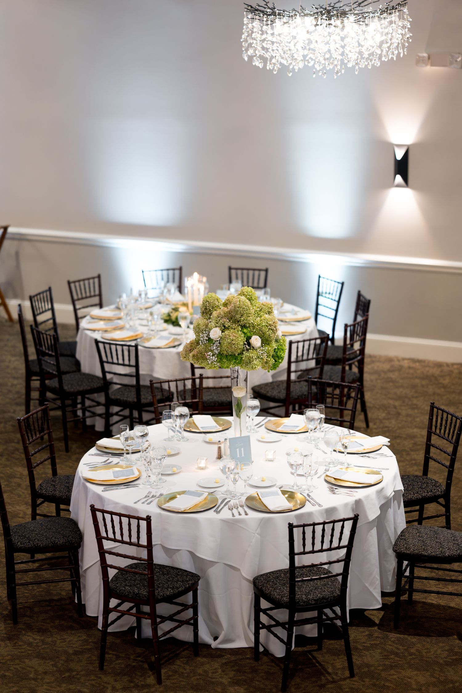 Formal wedding reception tables with crystal chandelier and hydrangea centerpieces.