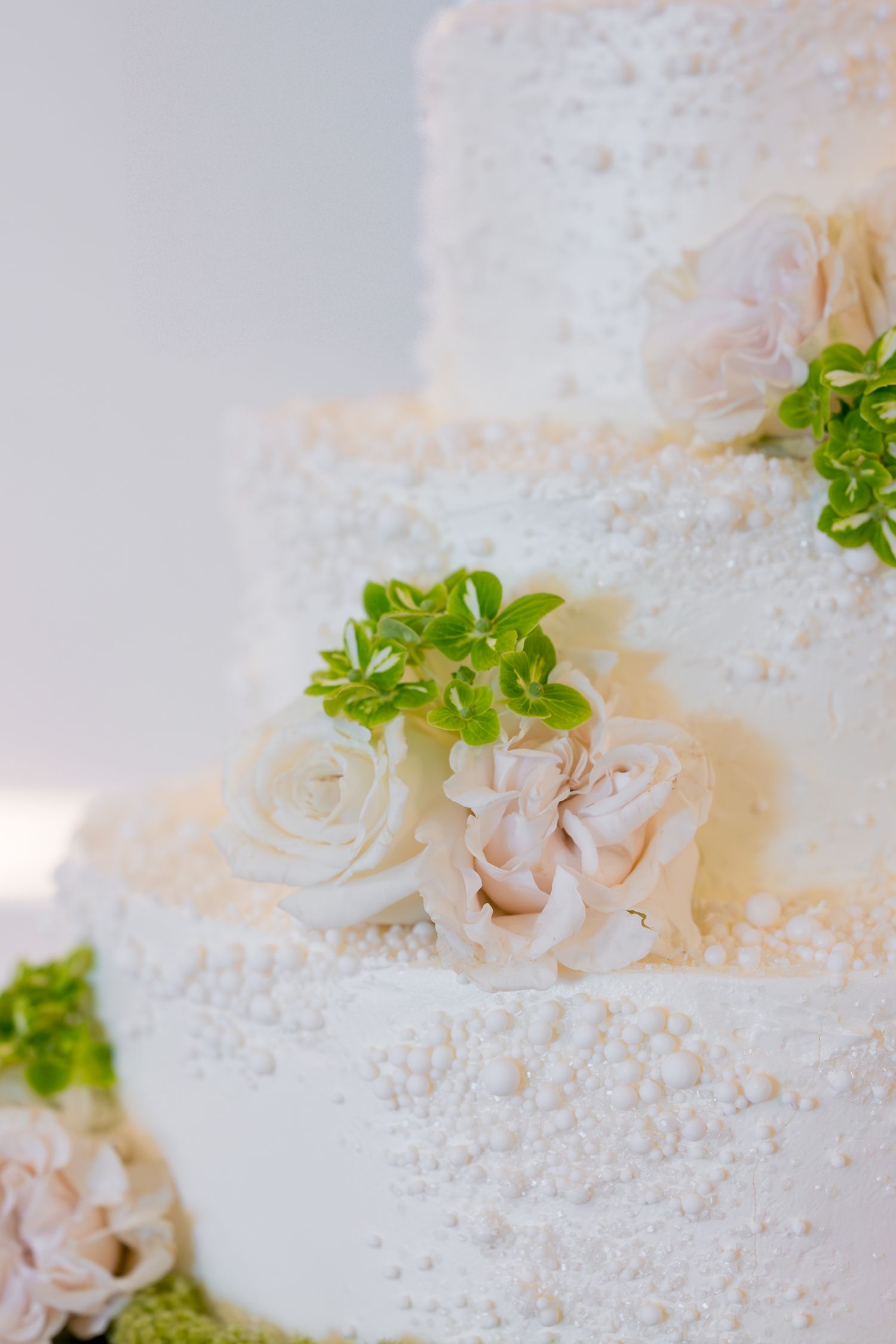 Elegant white wedding cake decorated with delicate roses and green accents.