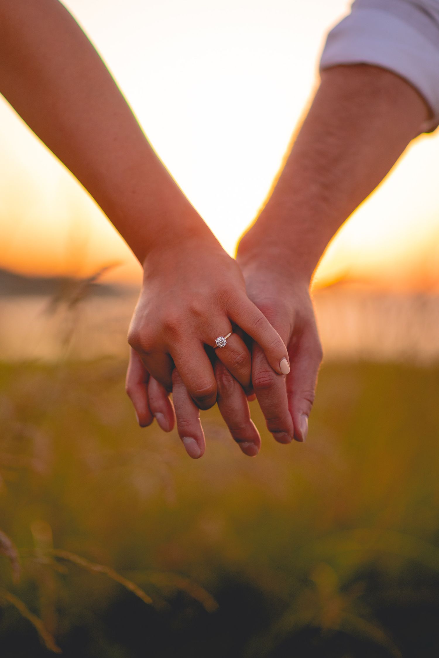 Close-up of two hands holding each other against a golden sunset backdrop.
