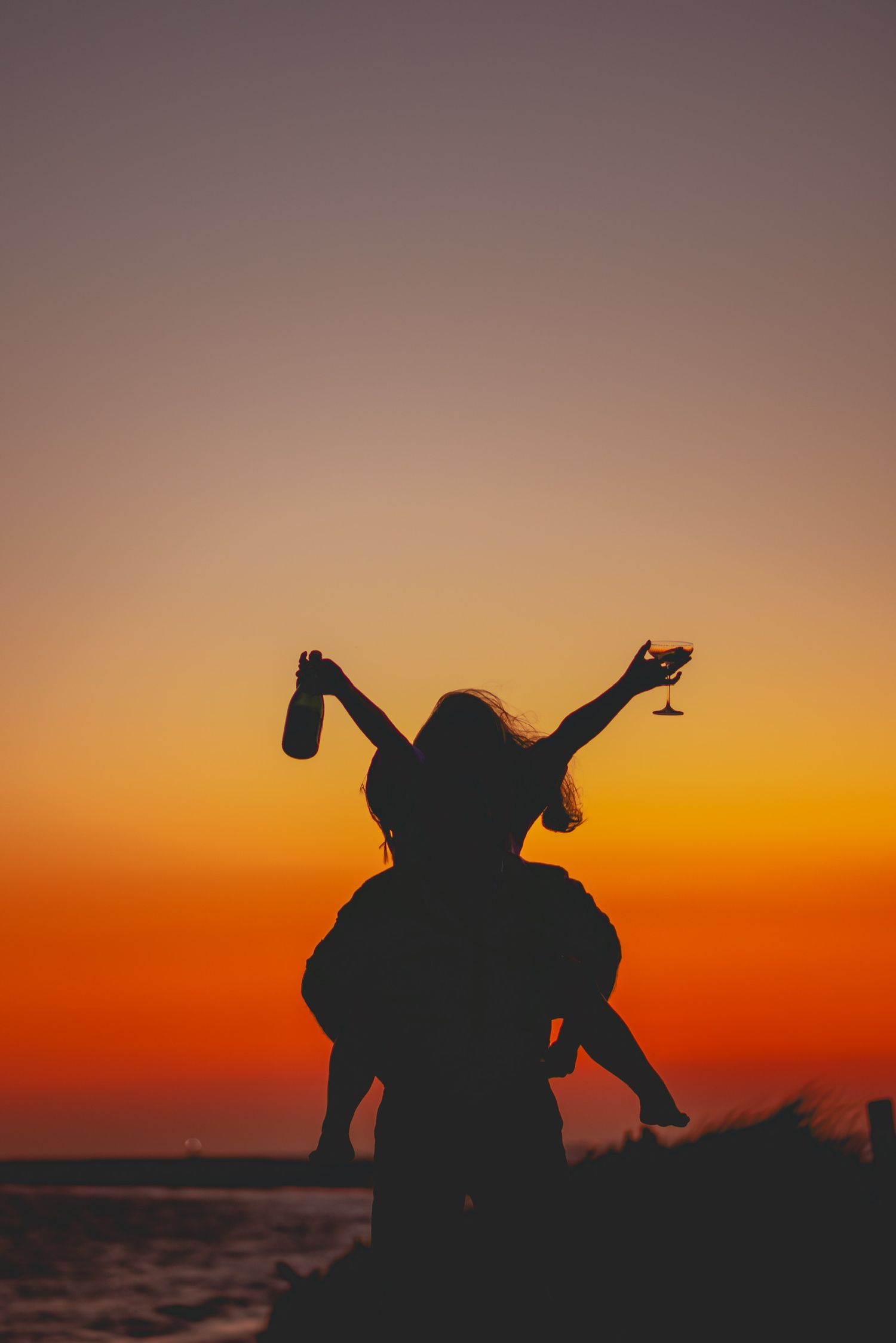 Silhouettes of two people sitting by the ocean during a dramatic sunset.