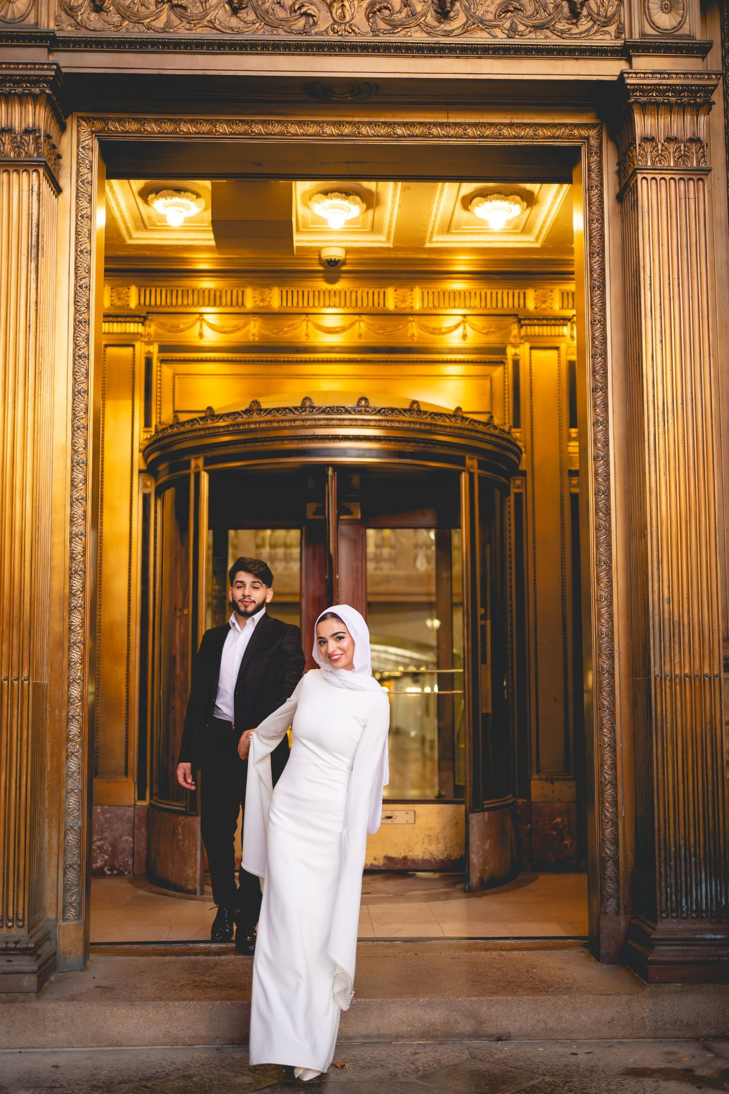 Elegant couple in white attire posing in front of ornate golden doorway at Hartford City Hall.