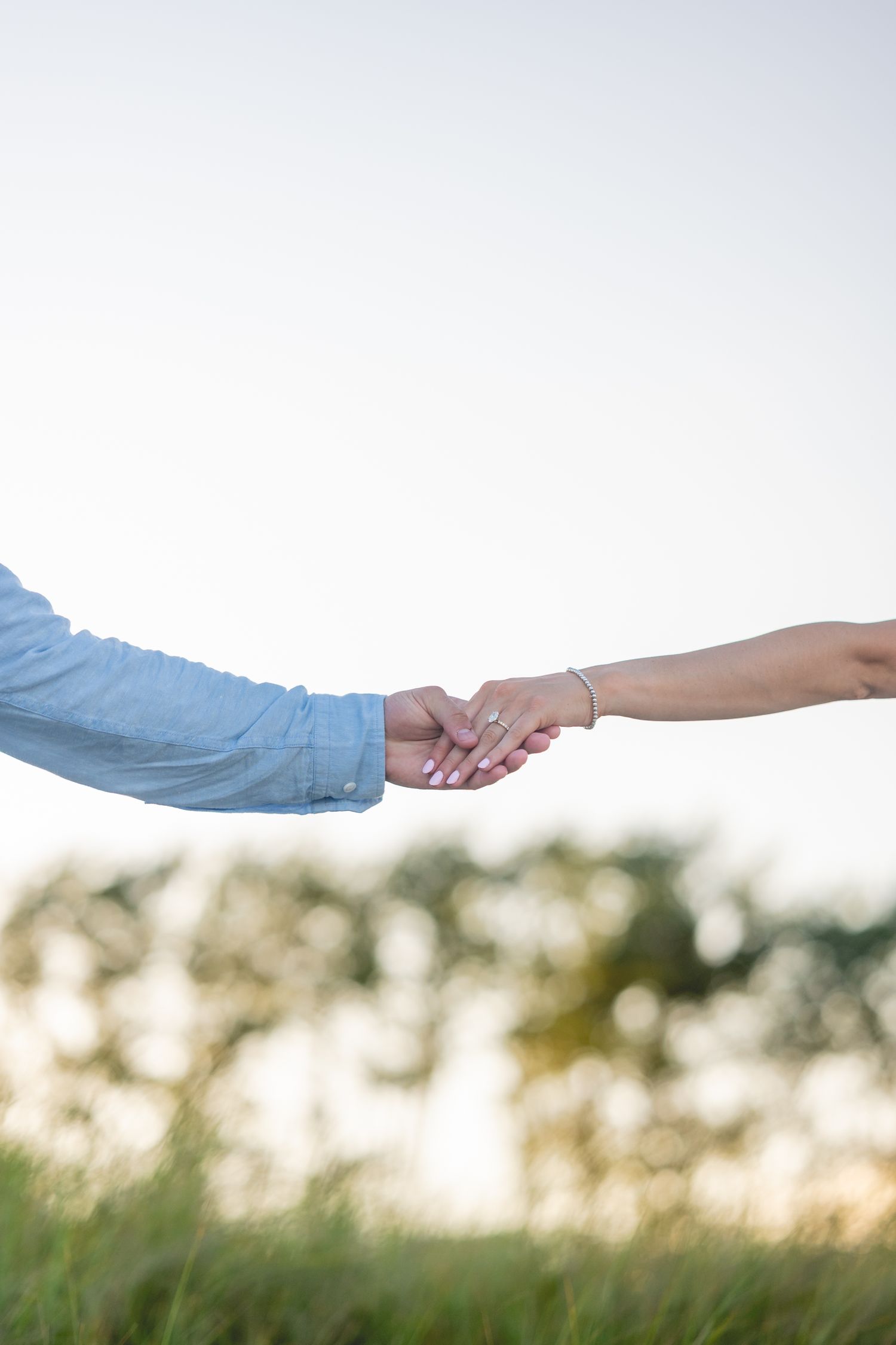 Close-up of two hands holding each other against a blurred natural background at sunset.