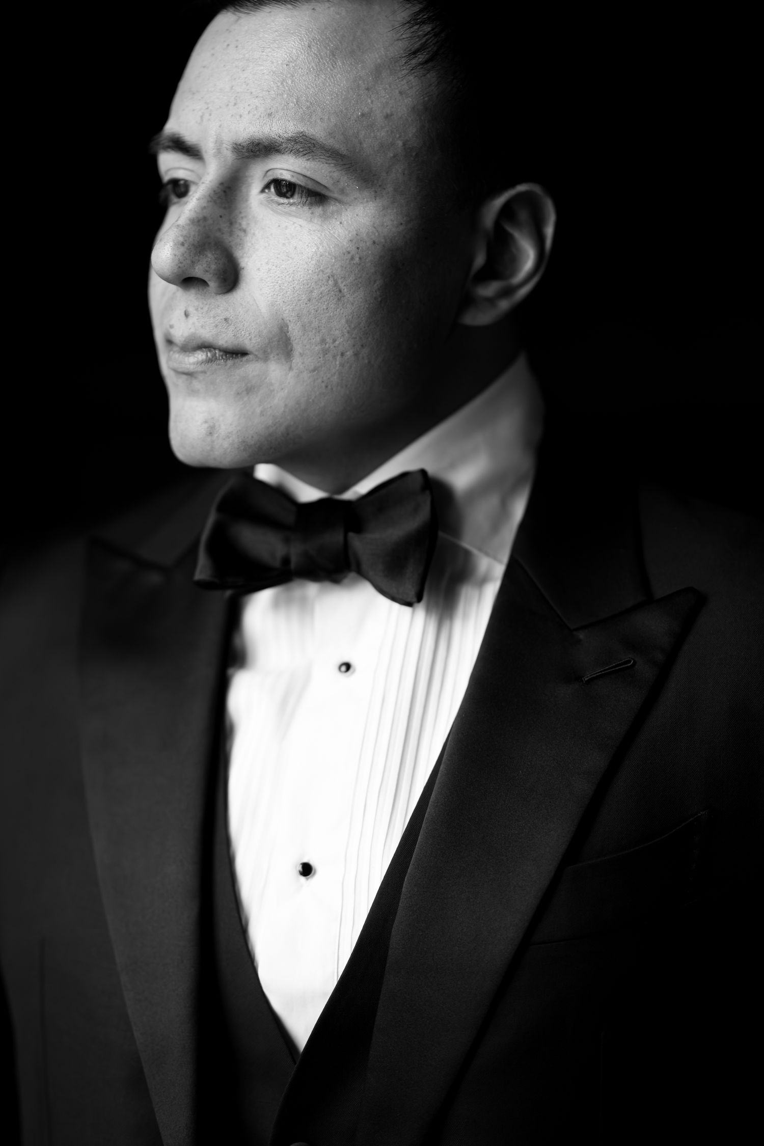 A dramatic black and white portrait series showing different angles of a person wearing a formal tuxedo with pleated shirt.