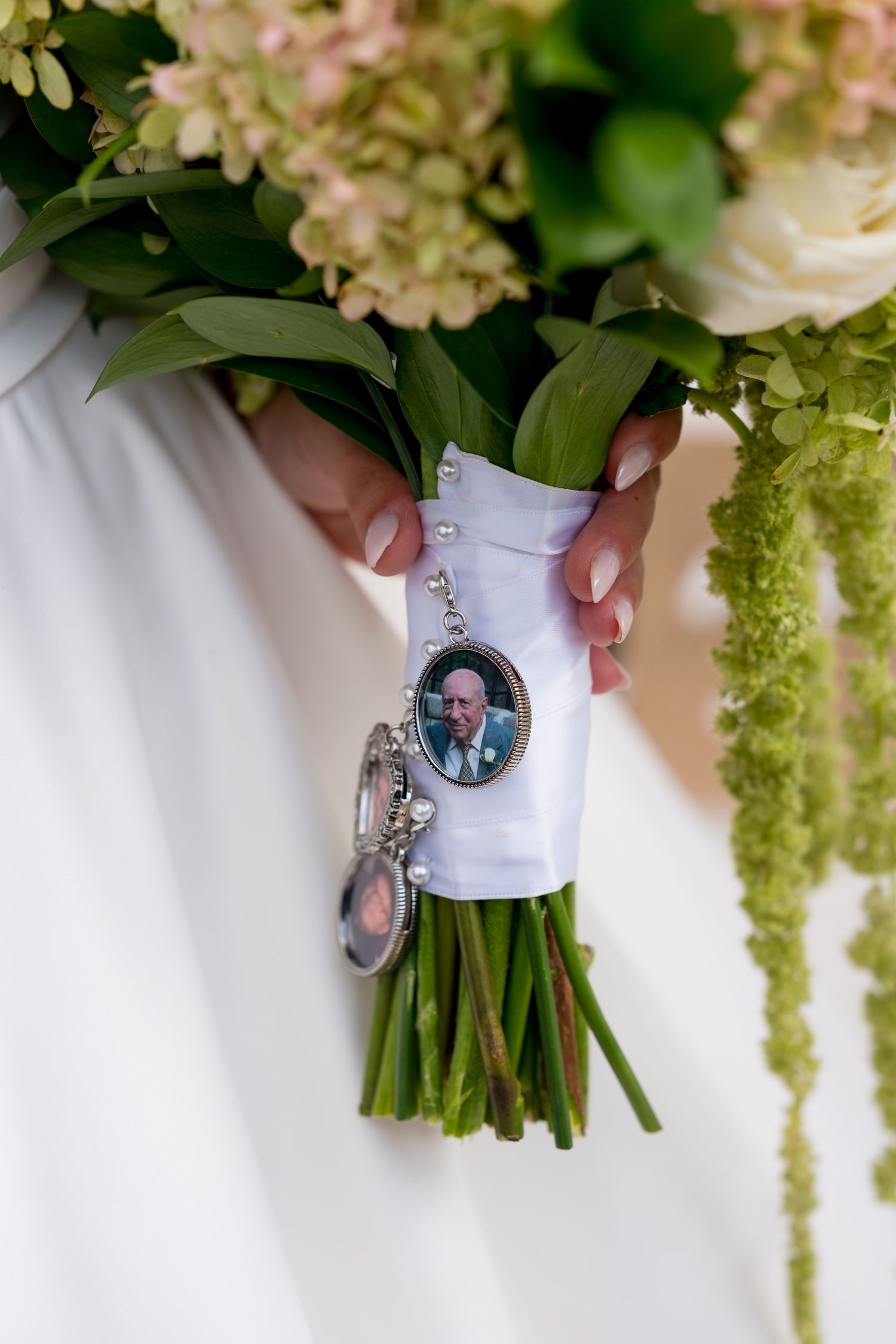 Wedding bouquet with pink and white flowers tied with a small photo charm attached to the stems.
