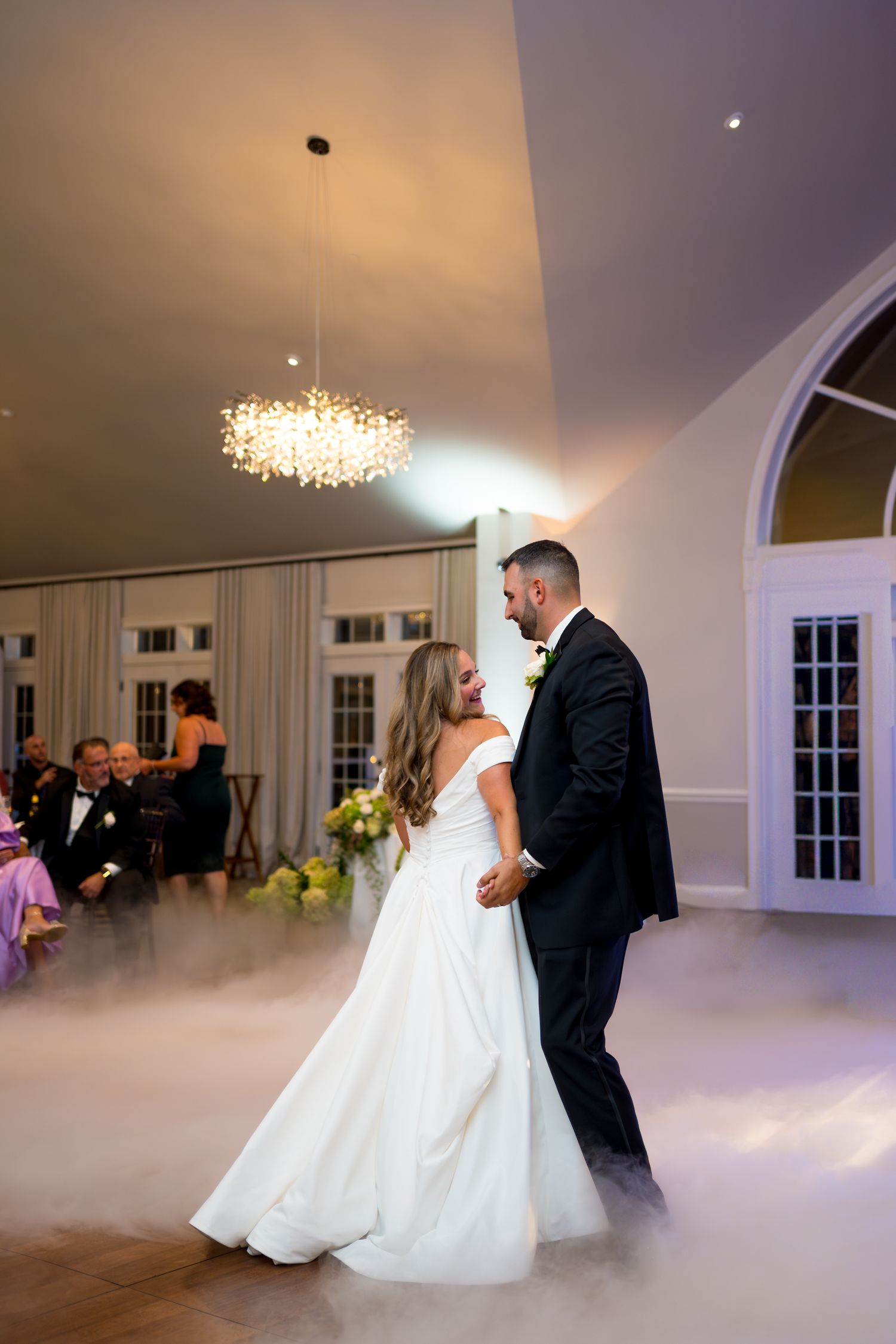 Couple dancing on a misty dance floor under crystal chandelier lighting at their wedding reception.