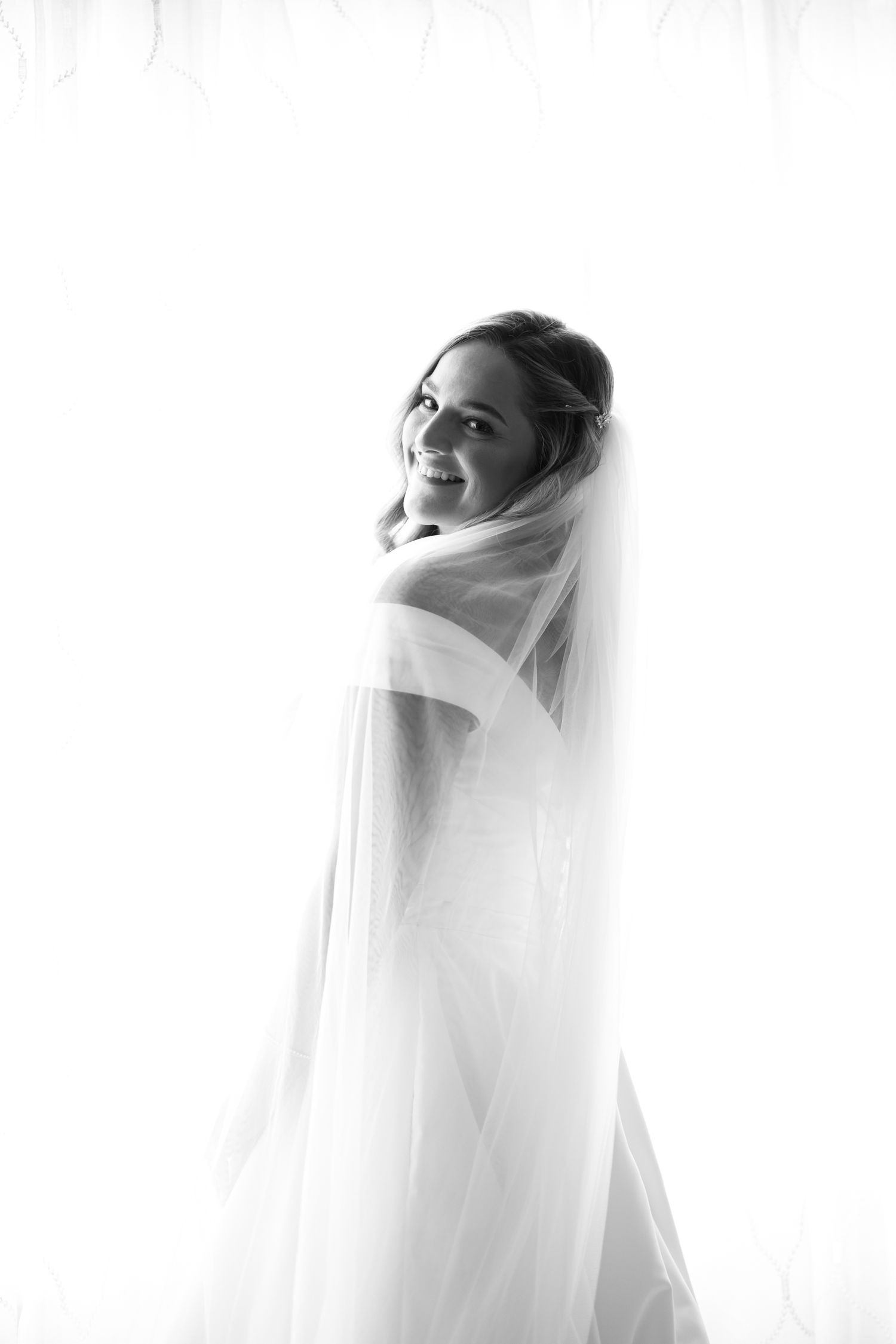 Artistic bridal portraits with flowing white veil against bright background.