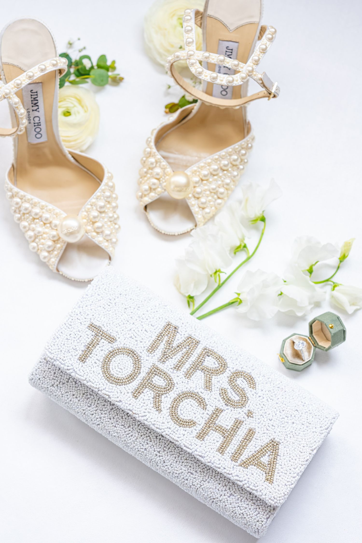 Pearl-adorned bridal shoes next to glittery wedding signage on white background.