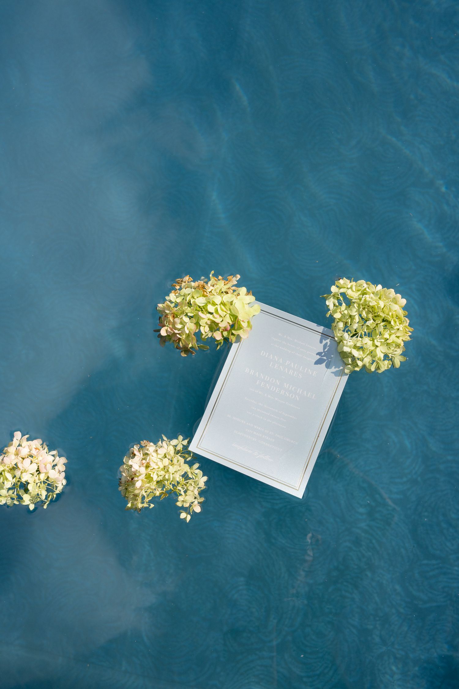 White invitation card surrounded by yellow hydrangea flowers on dark blue surface.