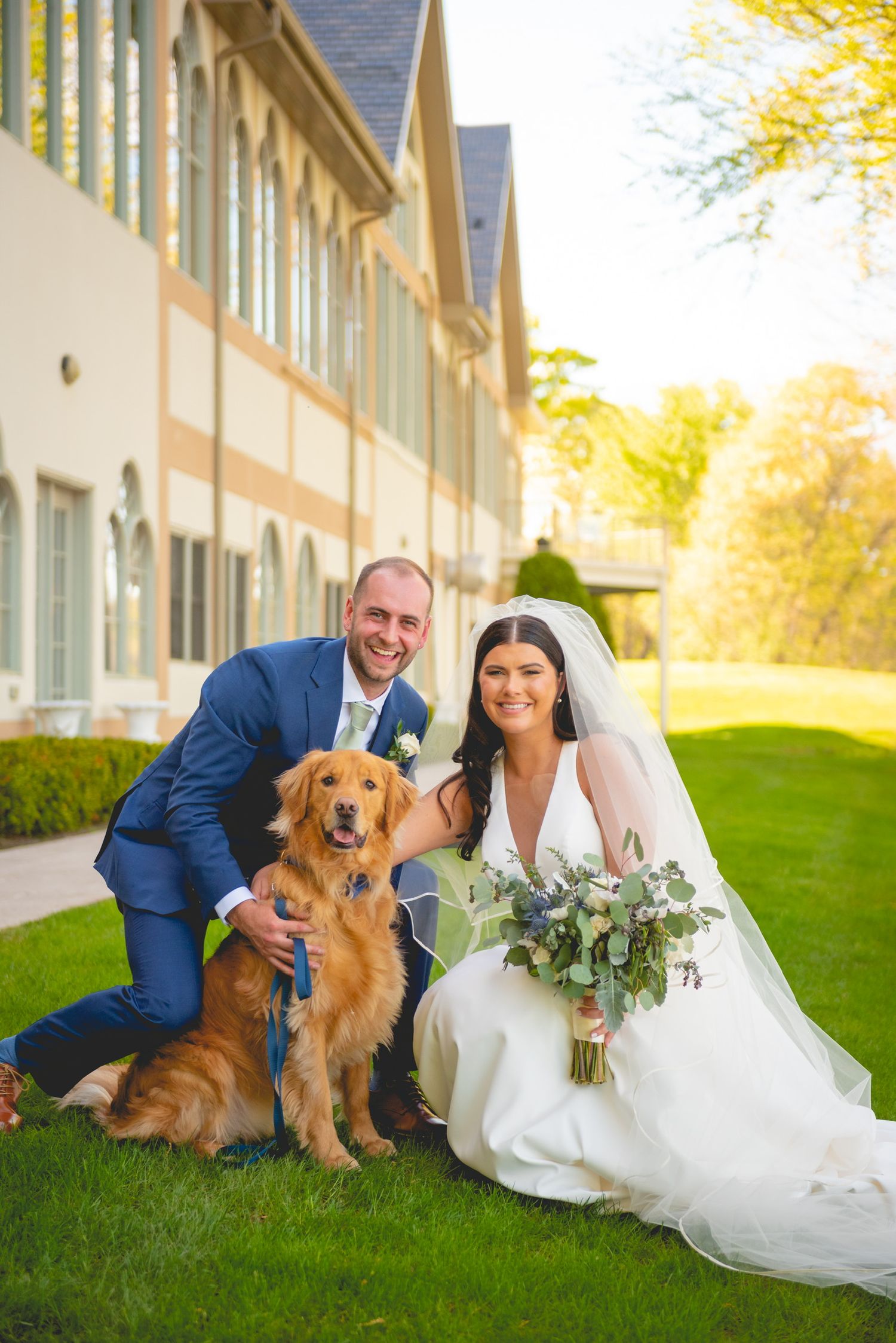 Wedding couple poses on grass with their golden retriever in formal attire.