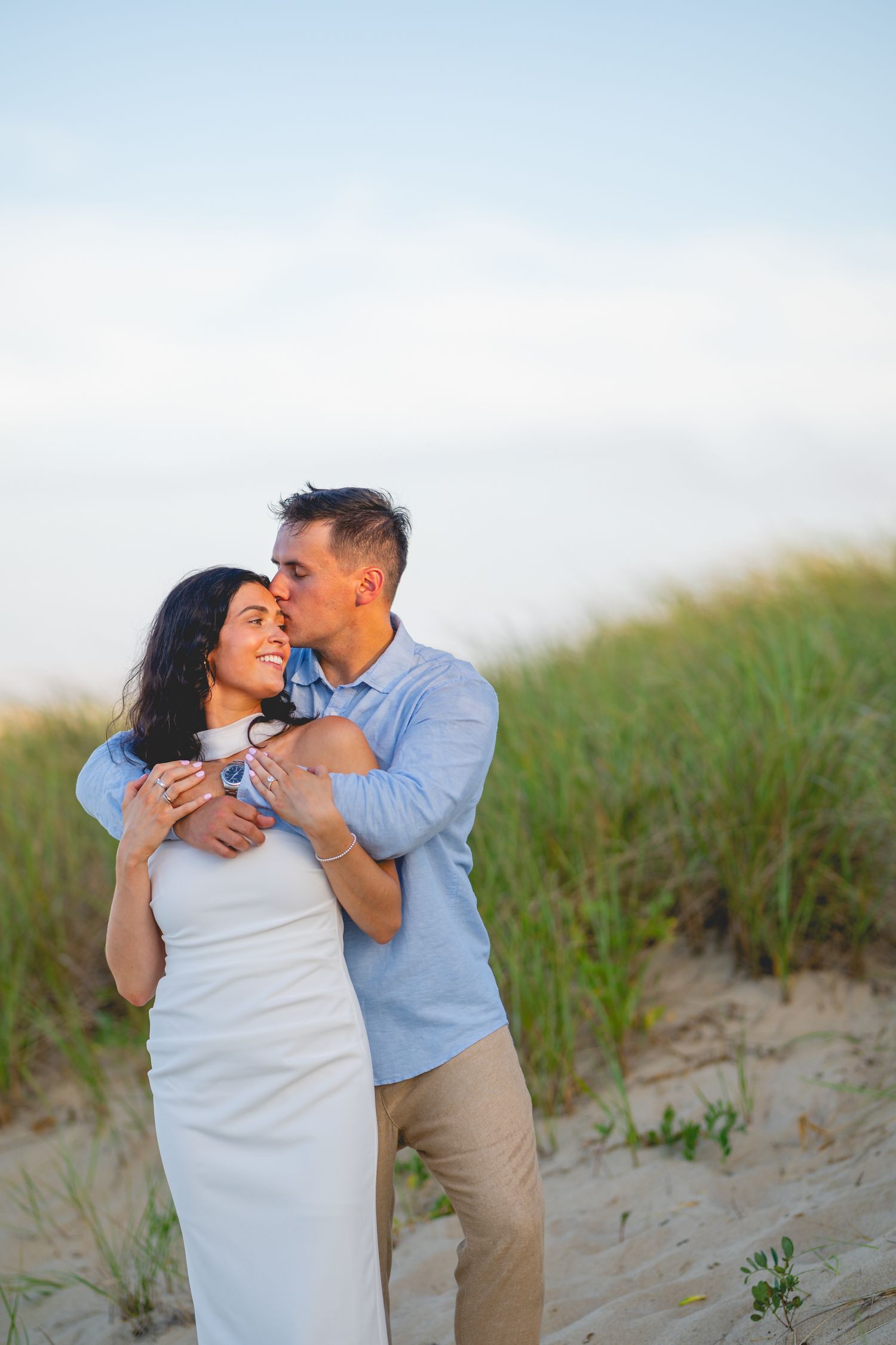 Couple shares intimate moments together on beach dunes with blue skies in the background.