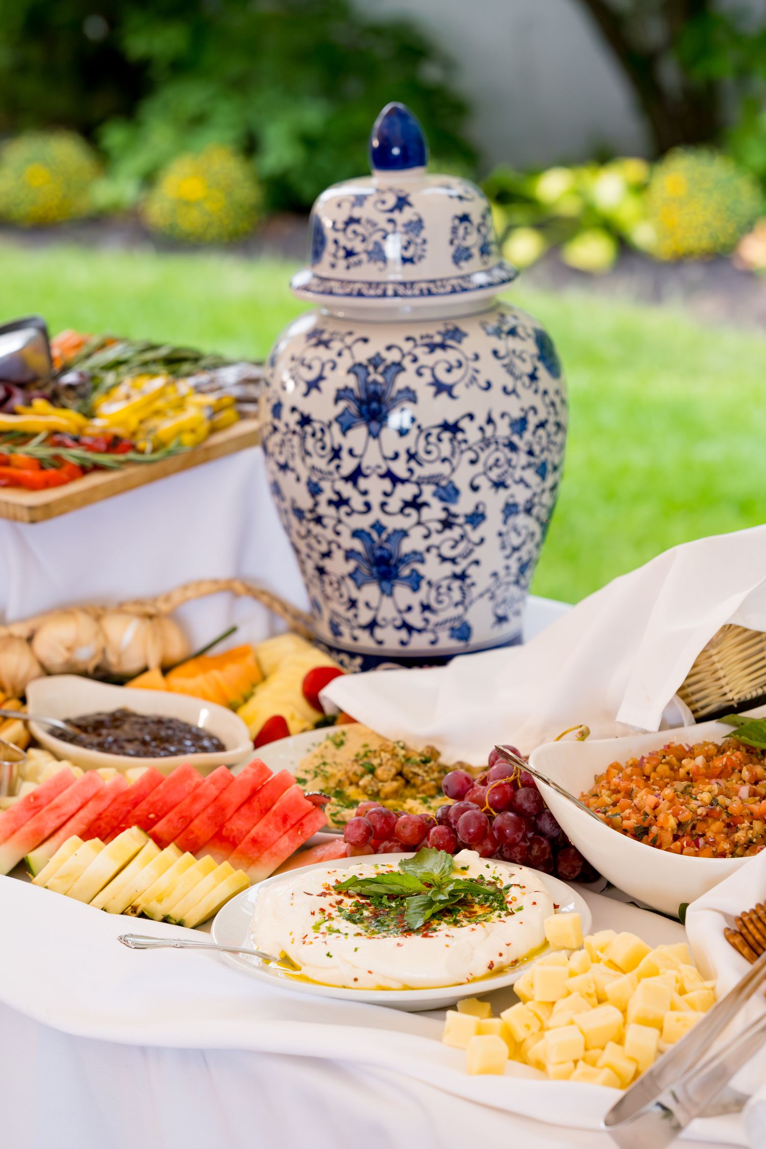 Elegant buffet spread with blue and white ginger jars featuring cheese, fruits, and appetizers.