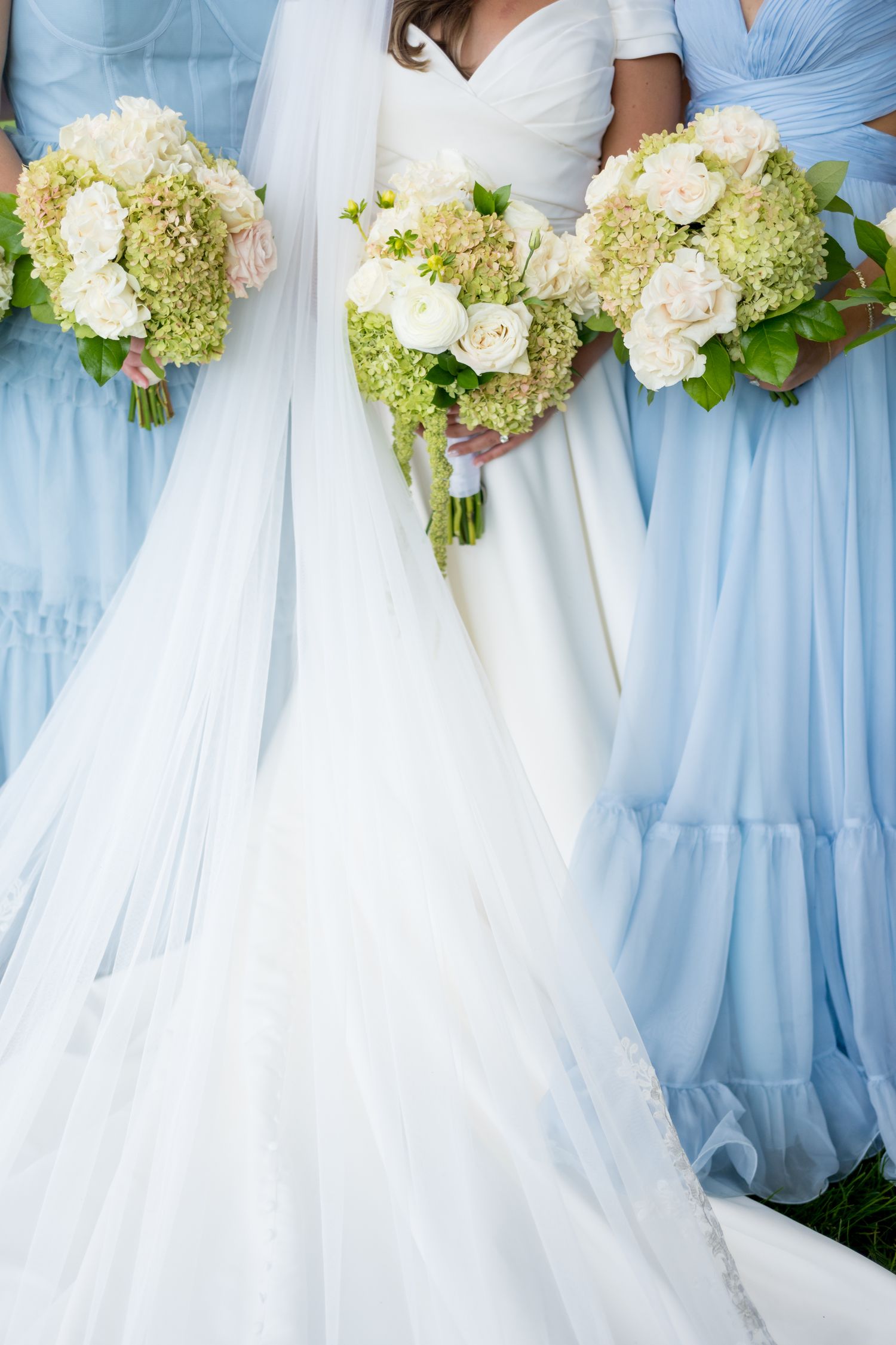 Wedding party detail showing light blue bridesmaid dresses and white hydrangea bouquets next to bridal gown.