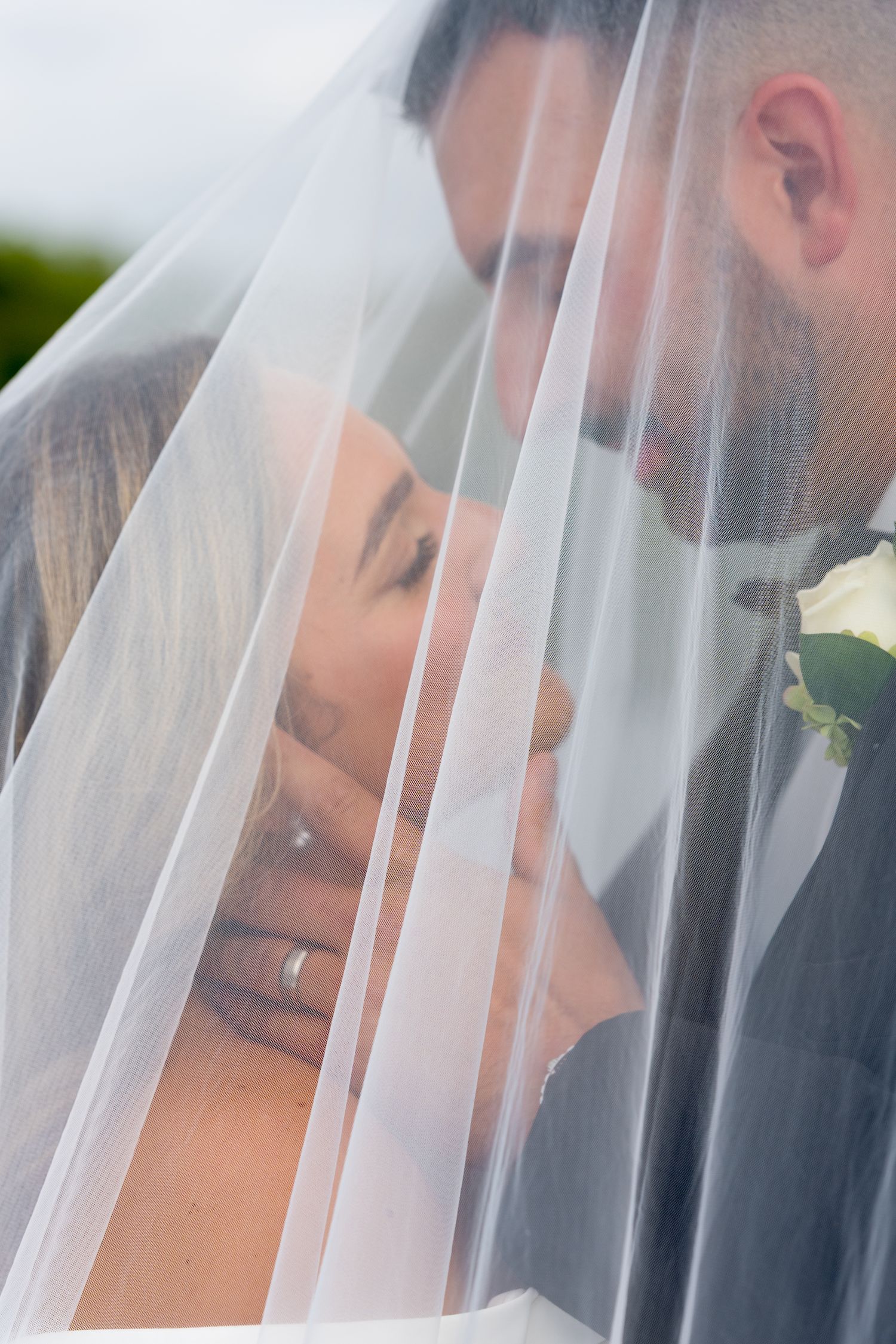 Romantic couple sharing an intimate moment under a delicate white wedding veil.