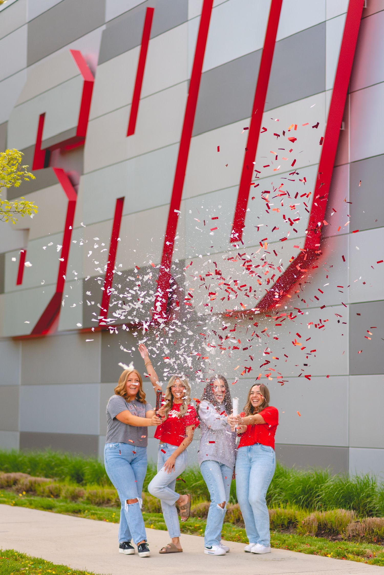 People in red shirts celebrating with confetti against a gray wall with red accents.