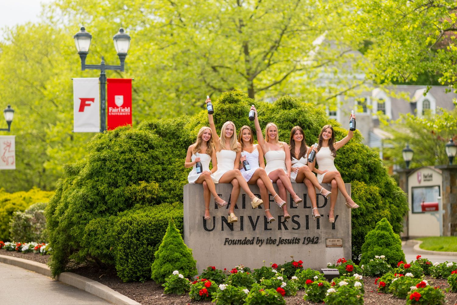 Fairfield university graduates on campus with green trees and signage in the background for graduation photos.