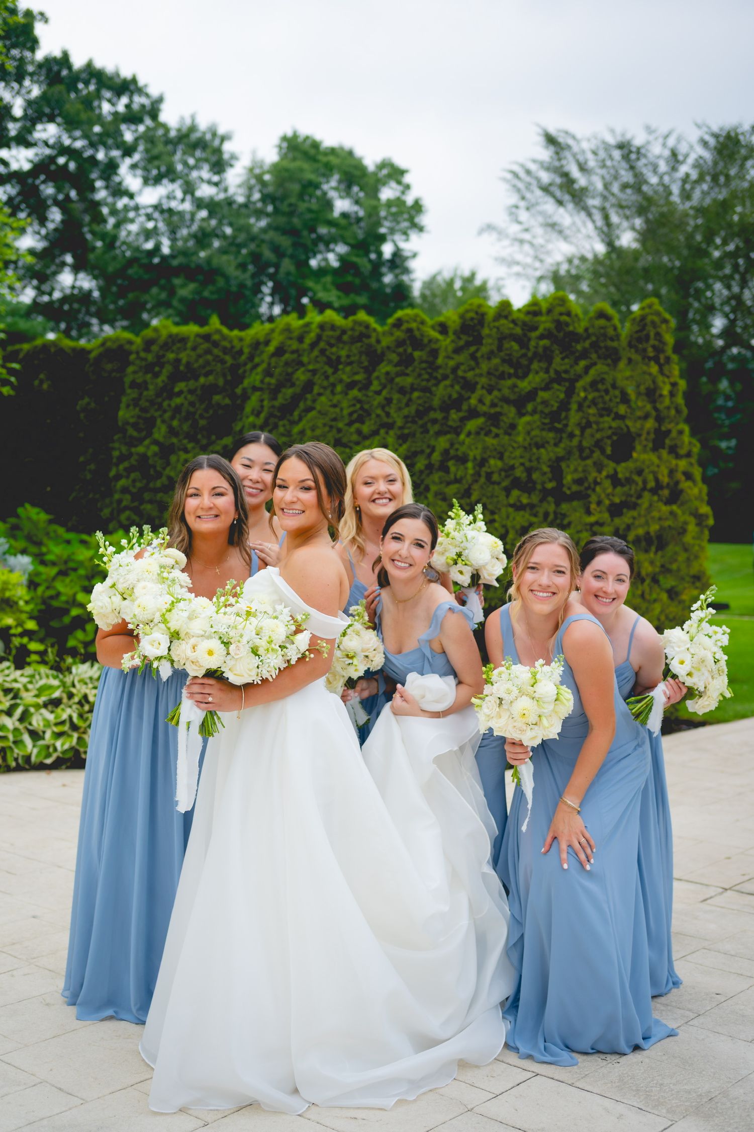 Wedding party in blue bridesmaid dresses and white gowns posing with bouquets.
