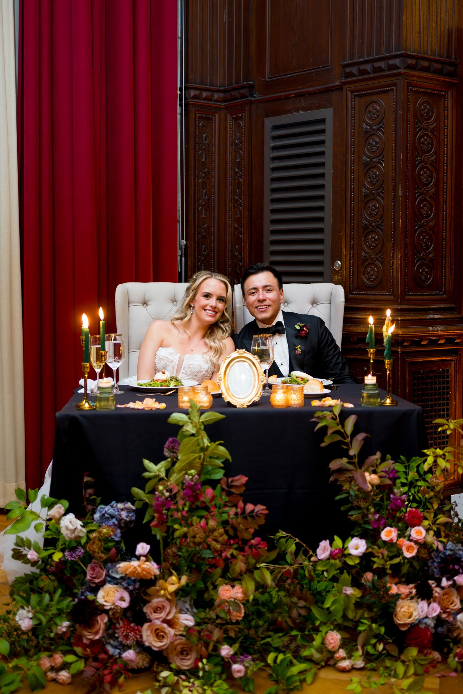 Elegant wedding reception table decorated with lush floral arrangements and glowing candles in an ornate venue.