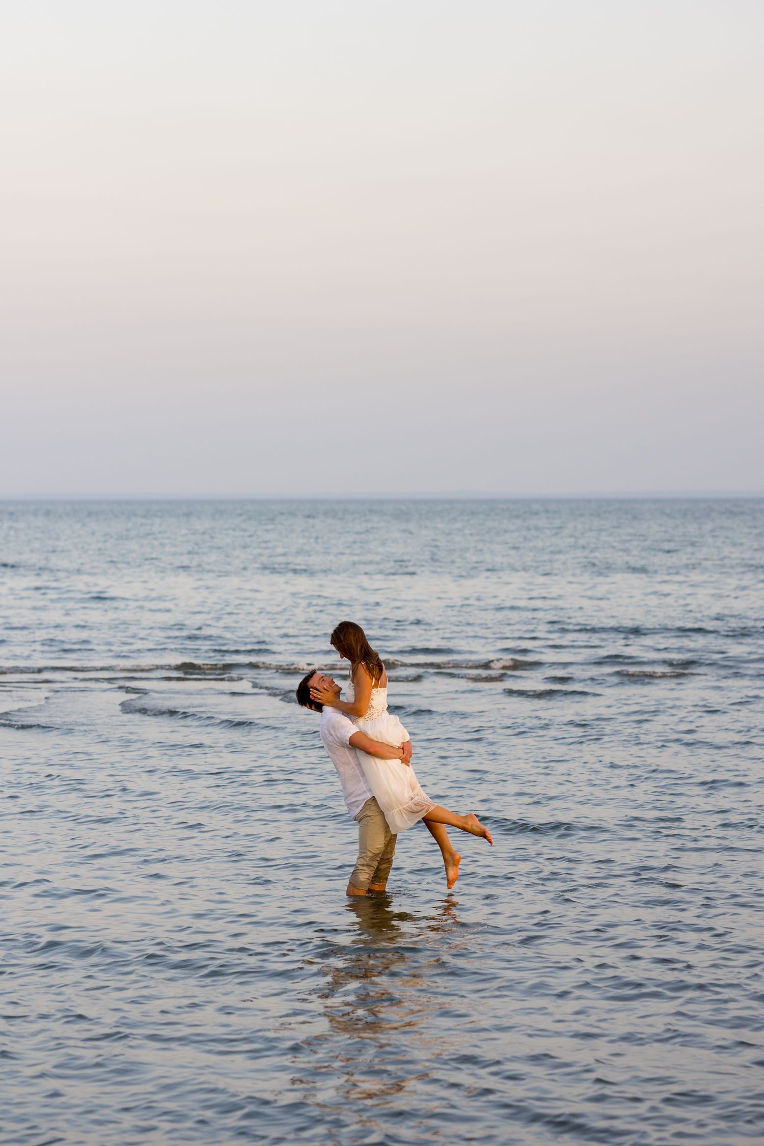 A couple shares an intimate moment while standing in shallow ocean waters at dusk.