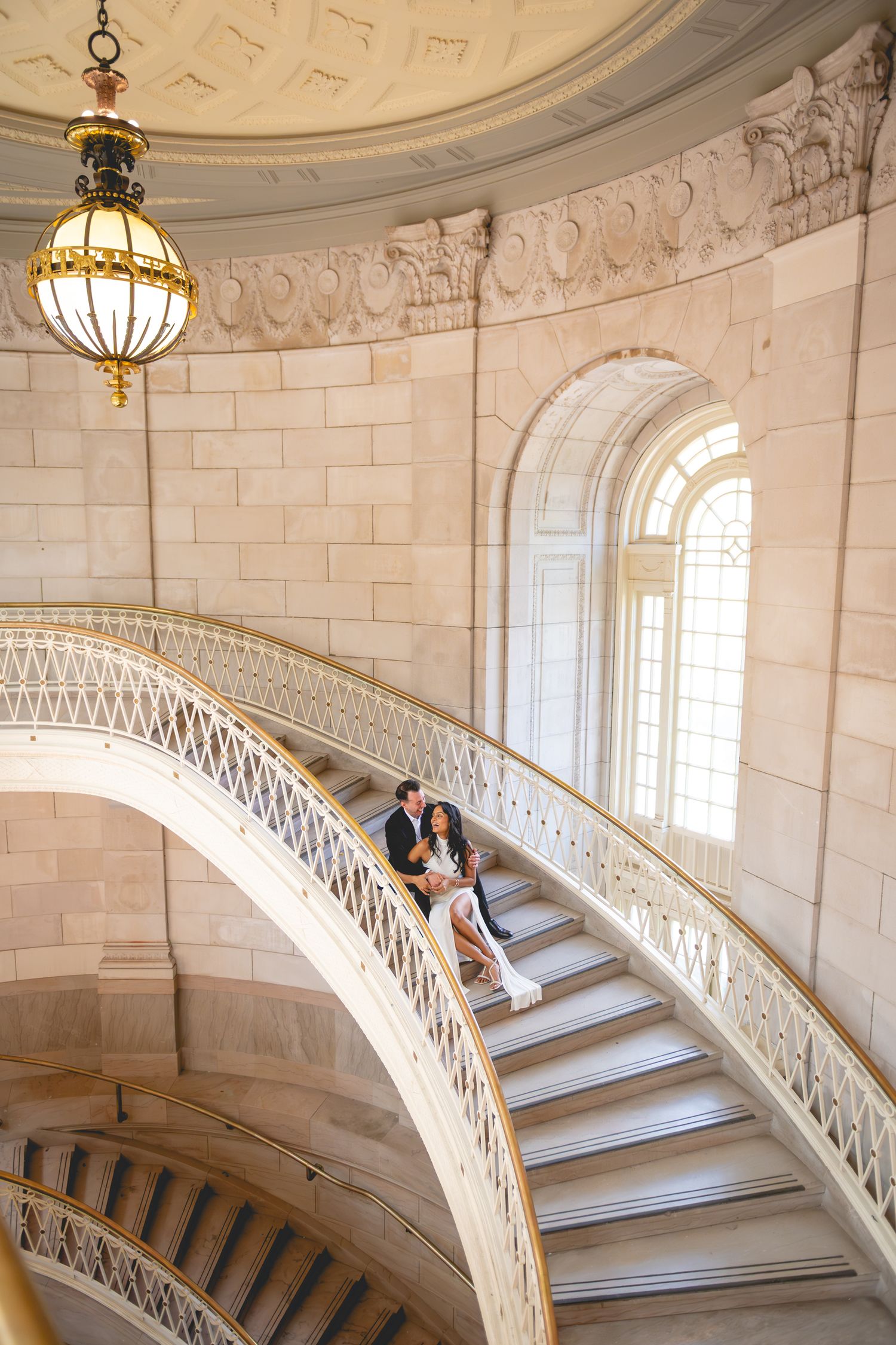 A couple shares an intimate moment on a grand marble staircase with ornate railings at Hartford City Hall.