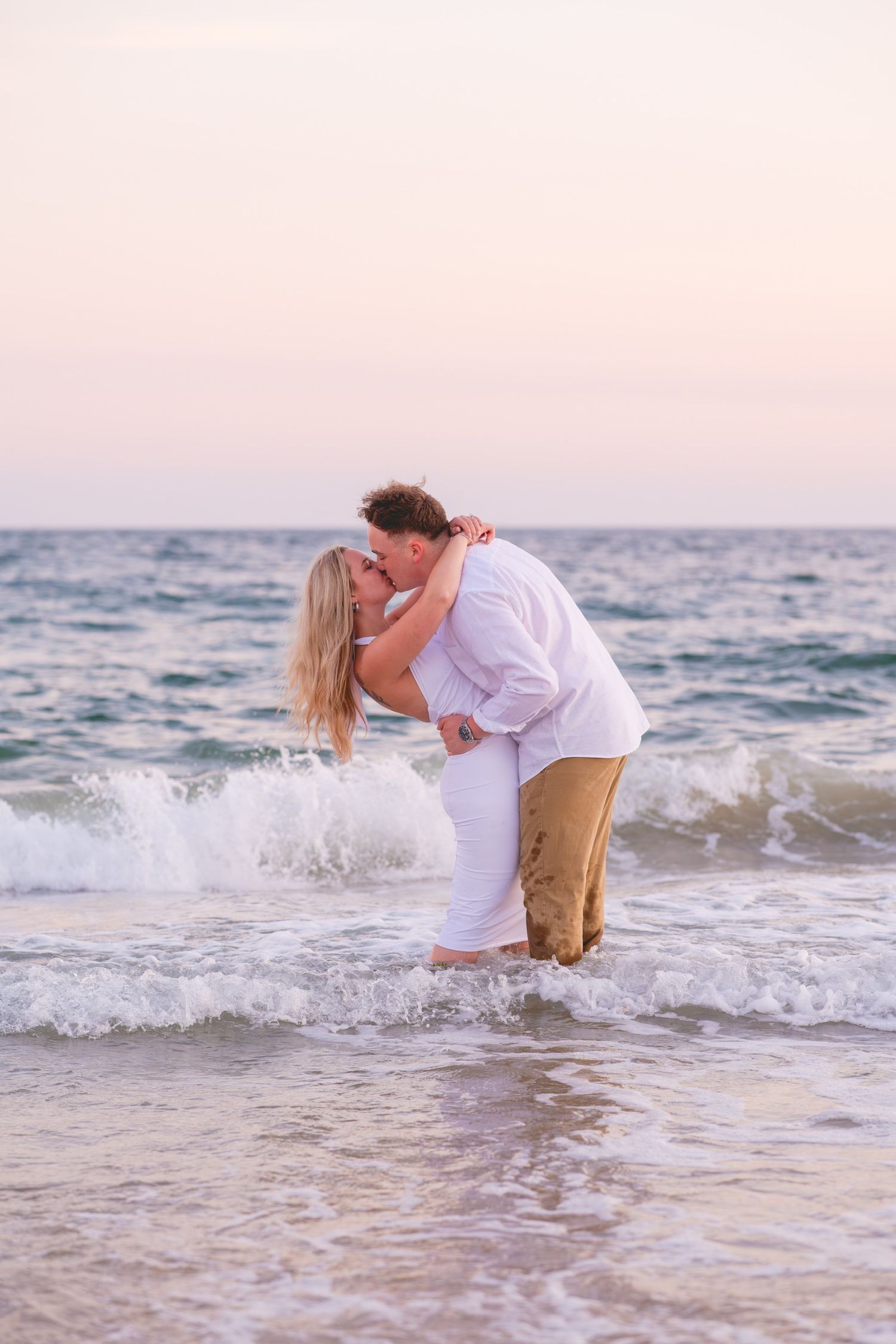 A romantic couple embraces in the ocean waves during sunset at the beach in Watch Hill, Rhode Island.
