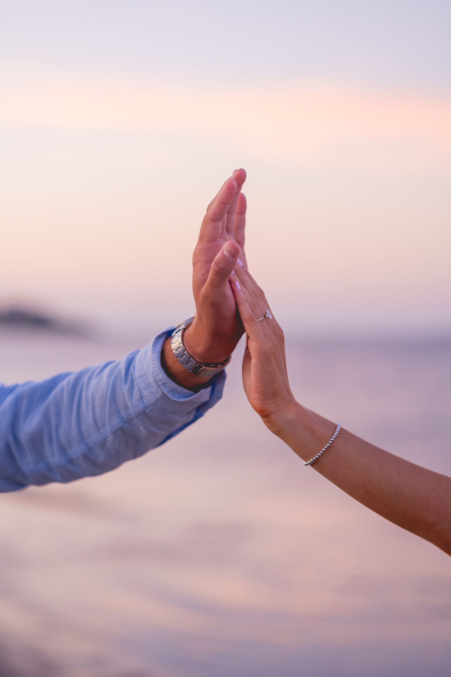 Two hands reaching out to touch each other against pink sunset sky over Cape Cod ocean.