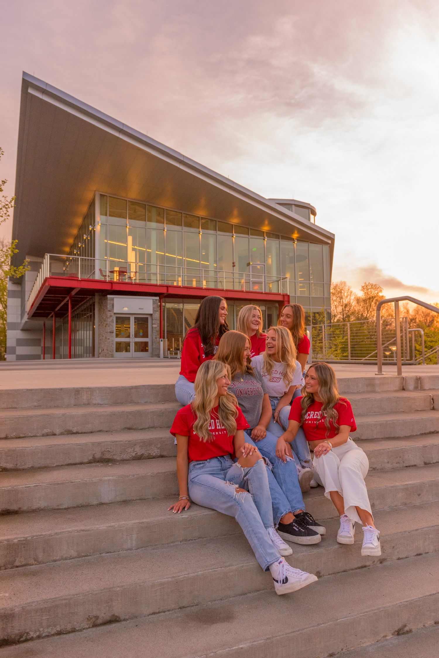 Sacred Heart graduates sitting on concrete steps at sunset wearing casual clothing for graduation photos.