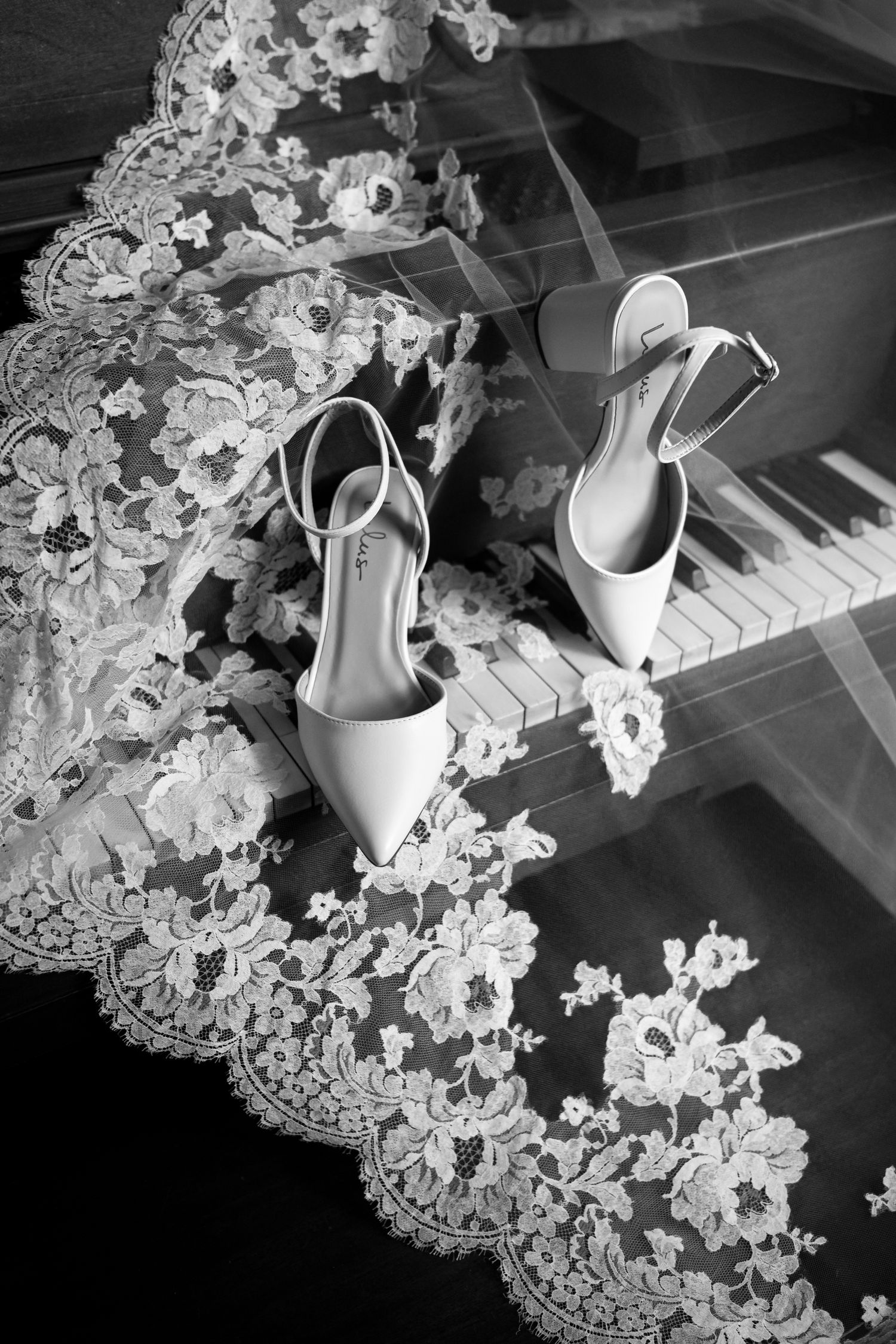 Wedding shoes and delicate lace veil arranged on piano keys in black and white.