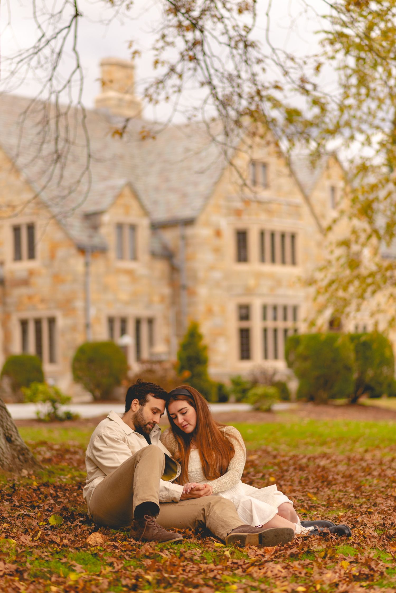 Couple relaxing on autumn leaves in front of grand stone mansion at Cranbury Park and Gallaher Mansion in Connecticut.
