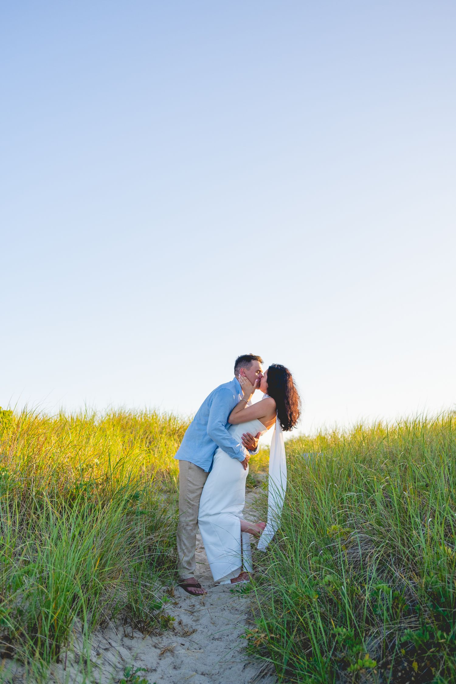 Couple sharing intimate moment among Cape Cod beach grass during golden hour.