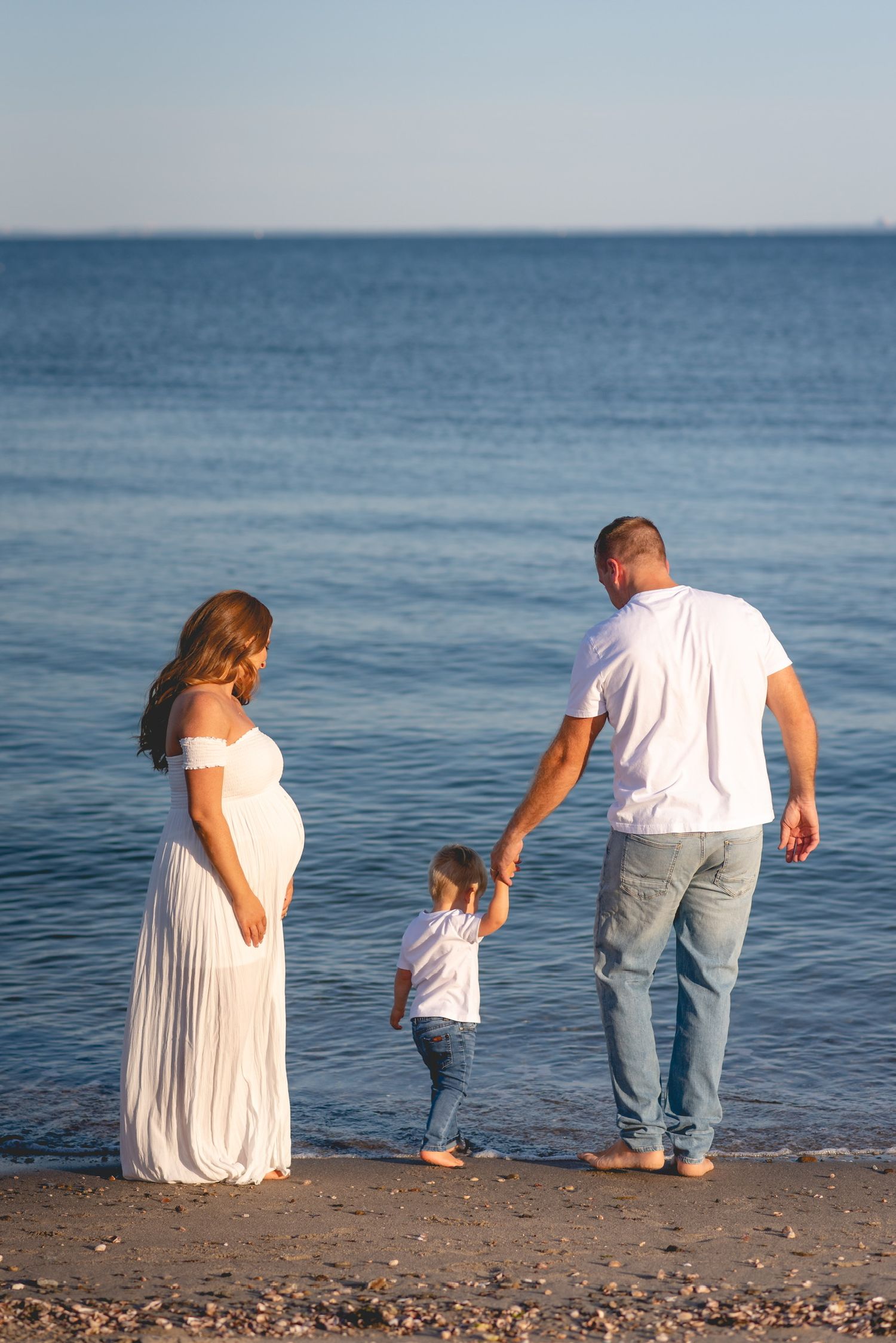 Family wearing white and jeans walking along a peaceful beach shoreline.