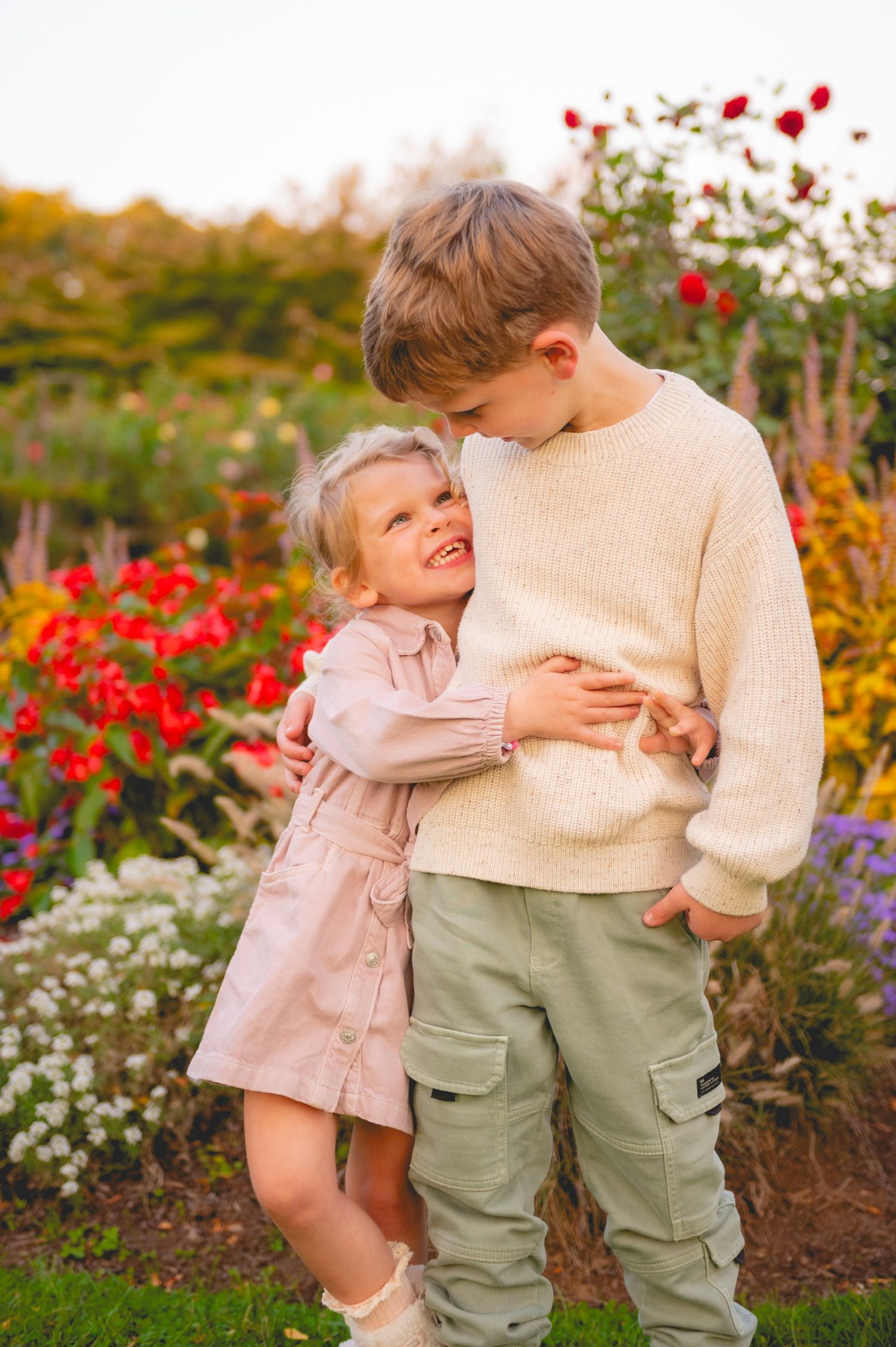 Two young children share tender moment in blooming flower garden.