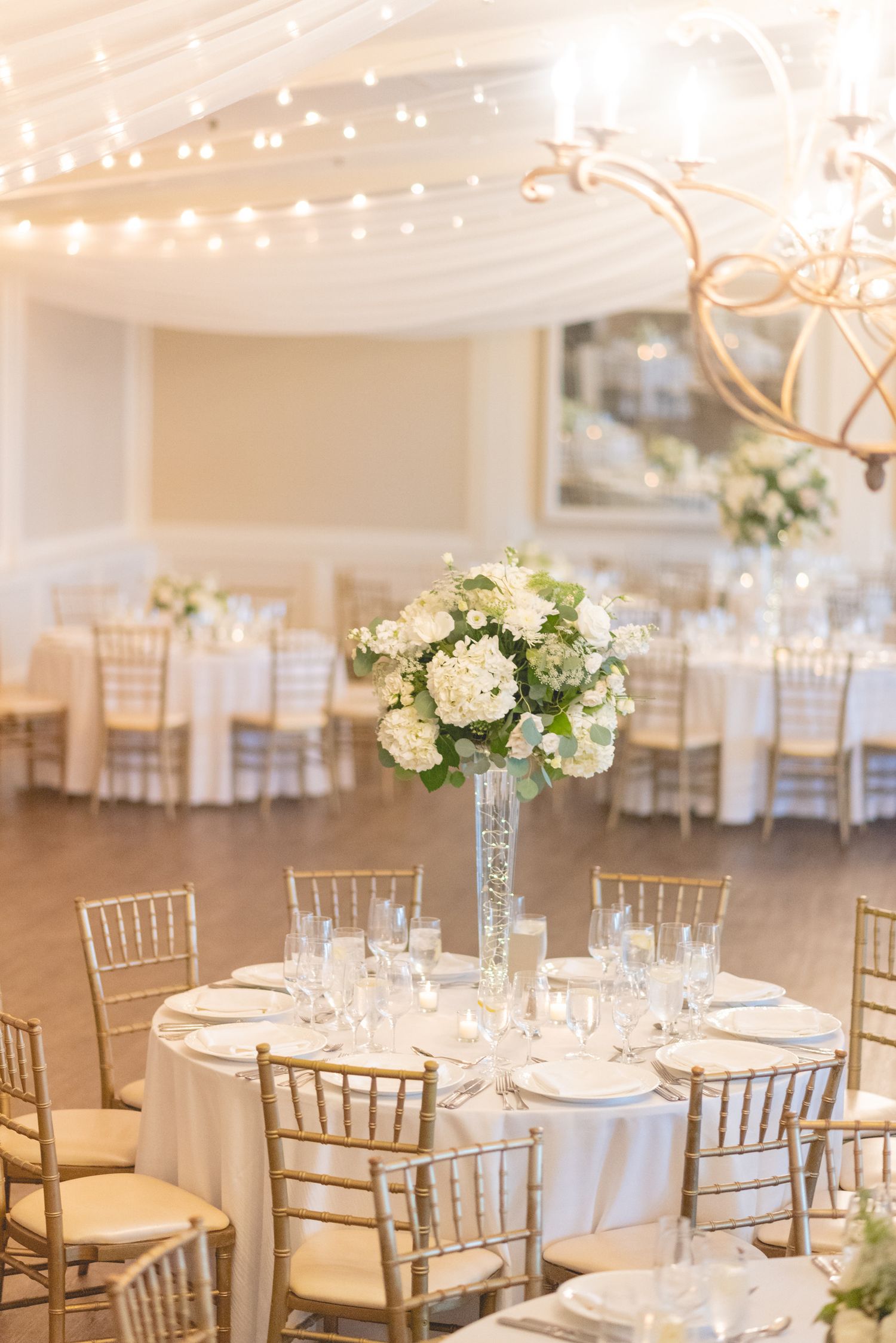 Elegant wedding reception venue with white floral centerpieces and gold chiavari chairs.
