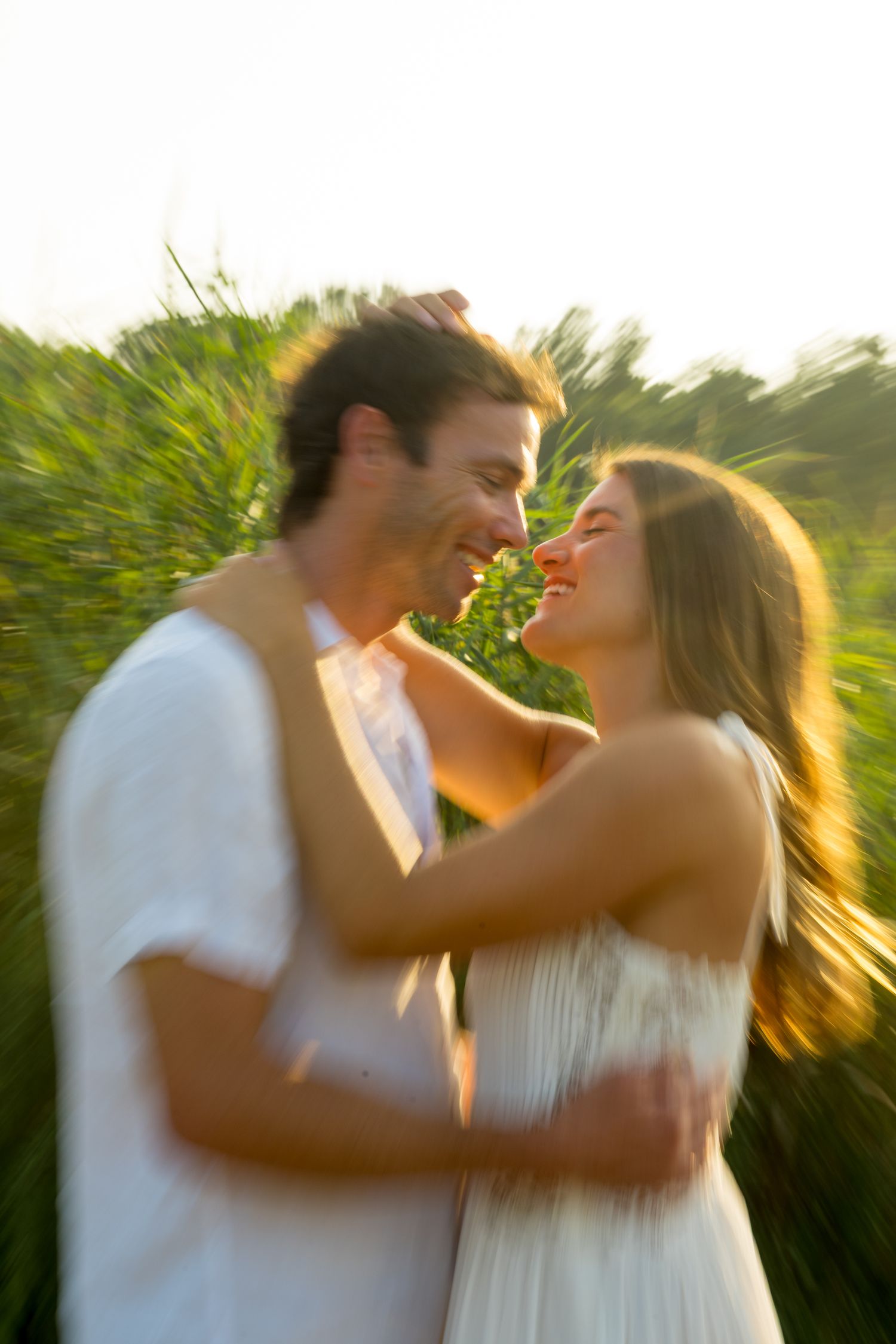 Intimate couple shares tender moment in sunlit field during summer photoshoot.