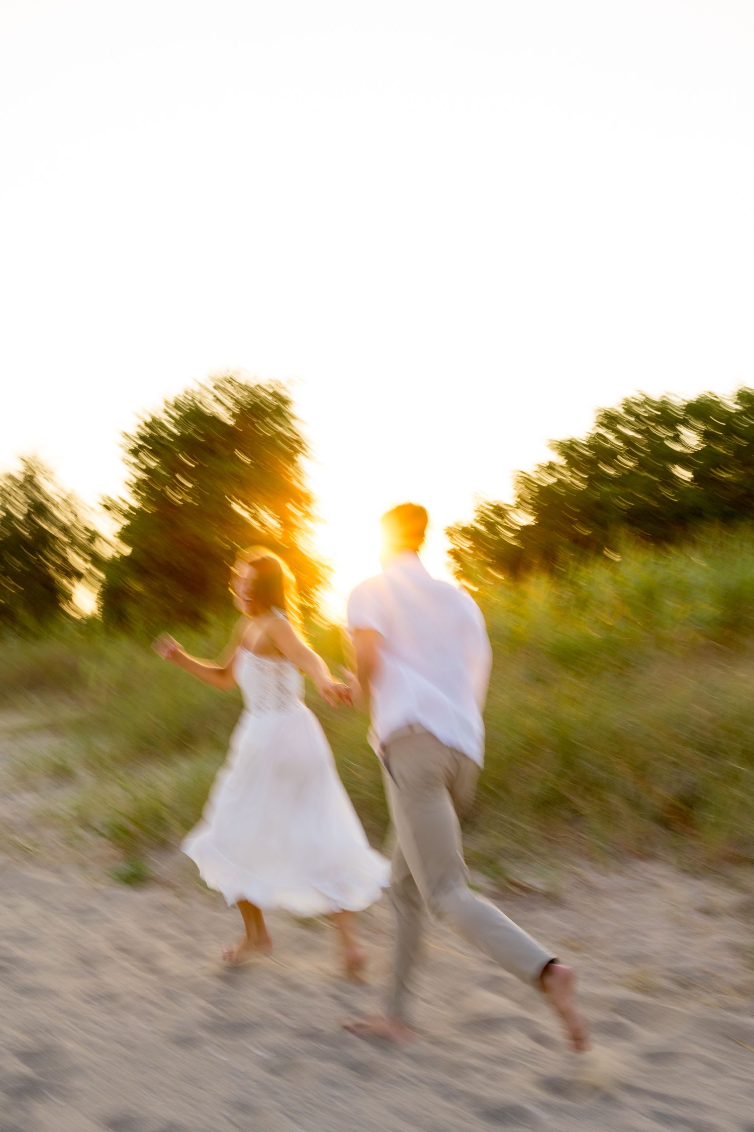 Silhouettes of a couple running and dancing on a beach during sunset with warm golden light.
