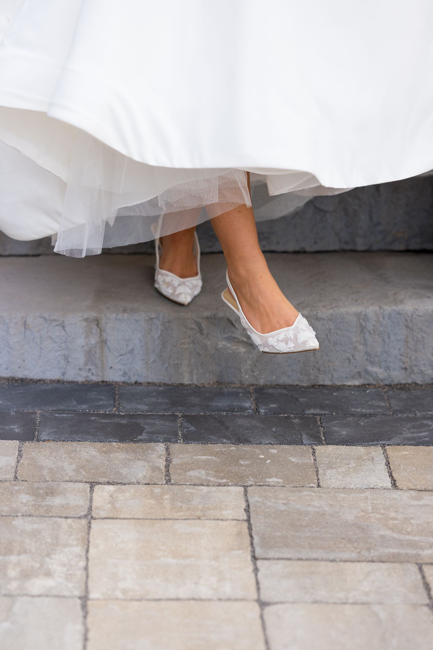 Close-up of white lace wedding shoes on stone pavement.