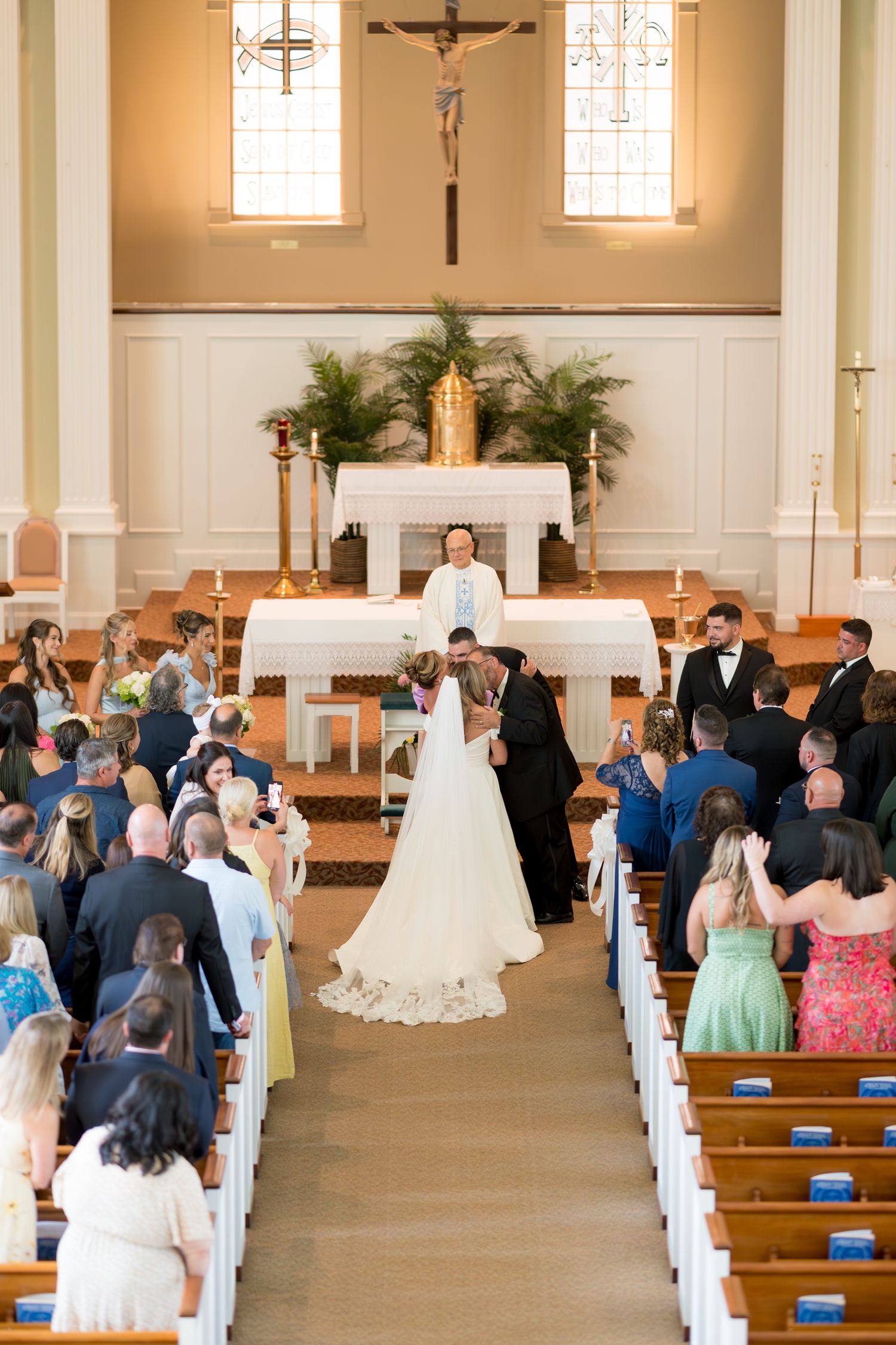 Traditional church wedding ceremony with guests seated in wooden pews and white floral decorations at the altar.